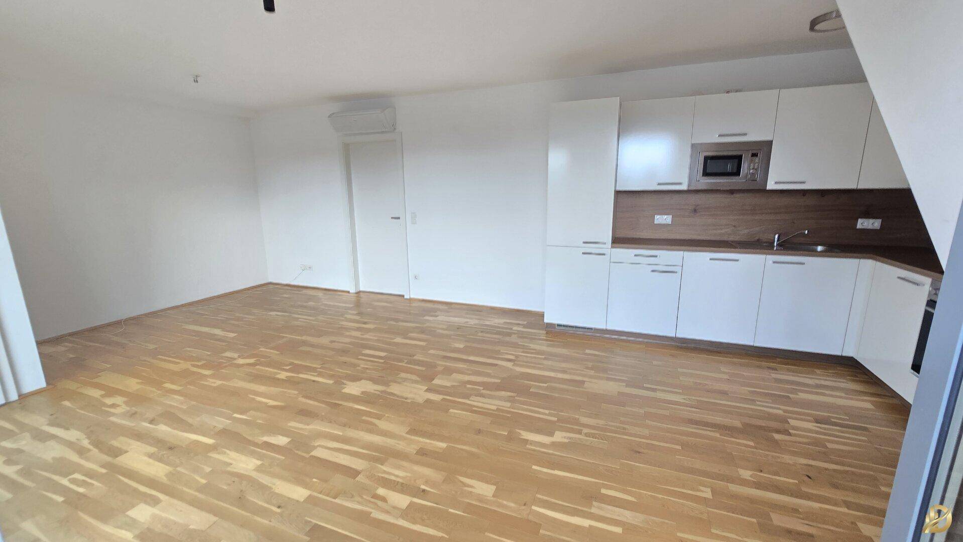 Moderner Wohnbereich mit integrierter Küche und Holzboden, viel Tageslicht für angenehme Atmosphäre.
