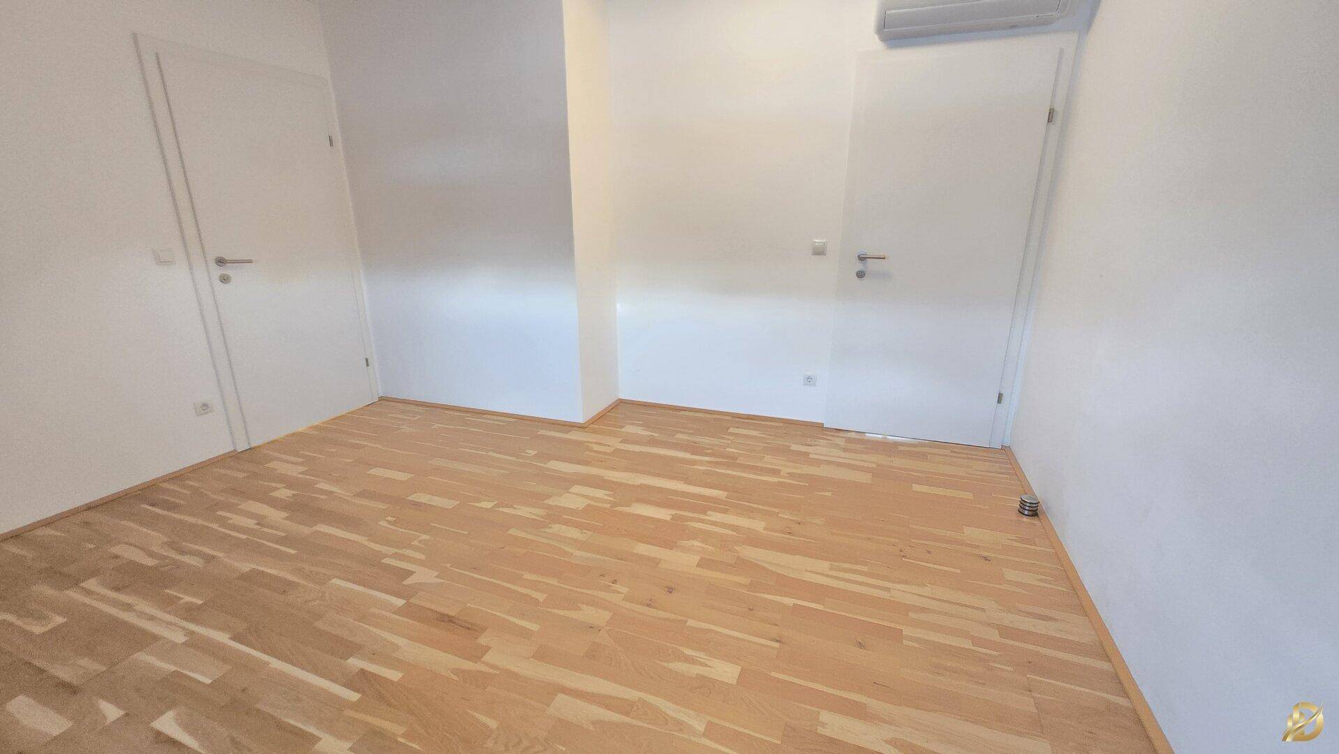 Helles Schlafzimmer mit Holzboden und weiß gestrichenen Wänden, bereit zur individuellen Gestaltung.