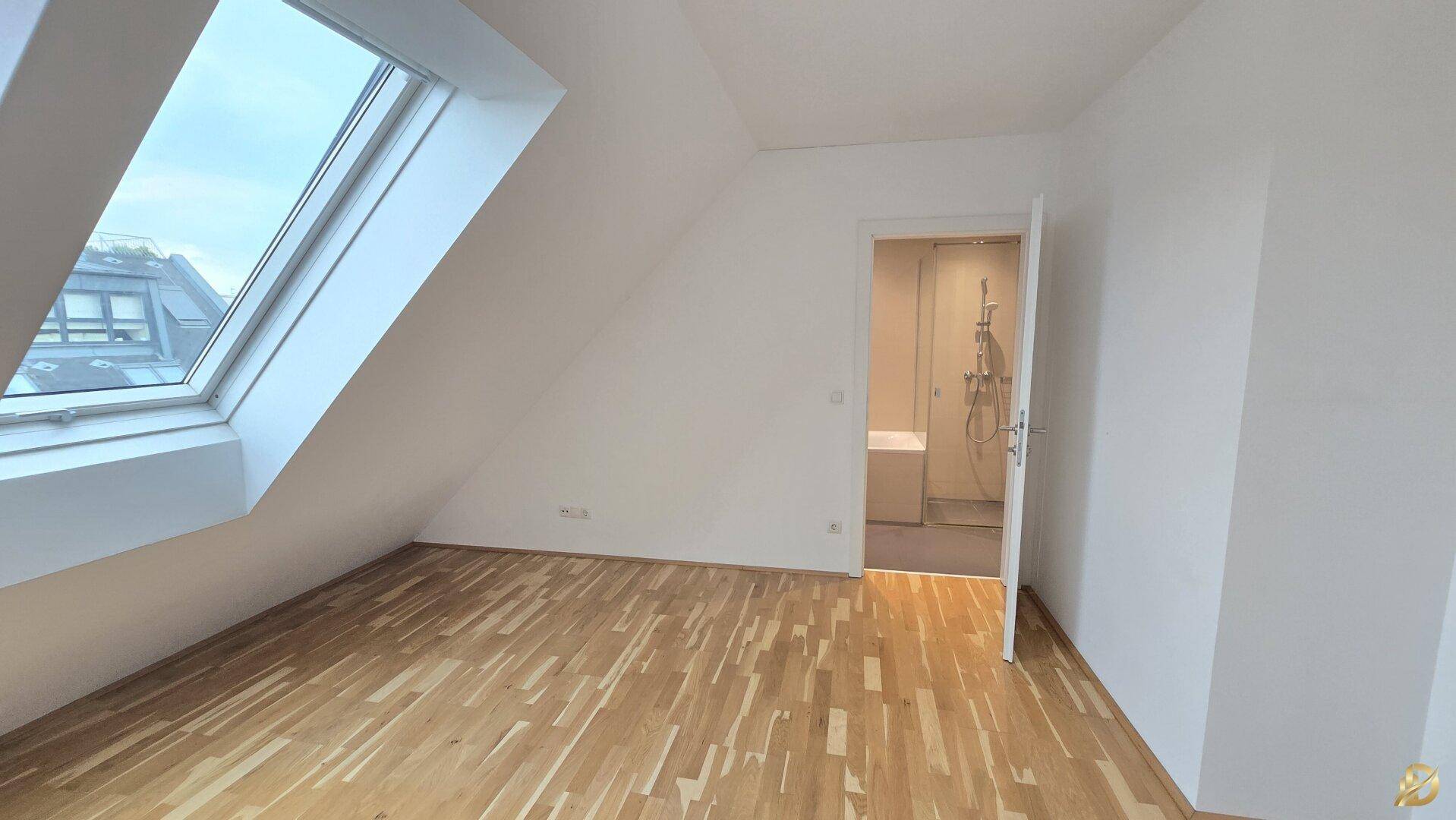 Schlafzimmer mit Holzboden und Dachfenster, mit Blick auf das angrenzende Badezimmer.