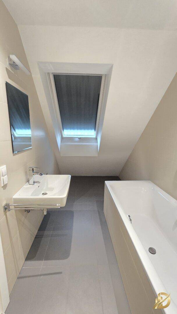 Helles Badezimmer mit Badewanne, Waschbecken und Dachfenster, modern gefliest und geräumig.