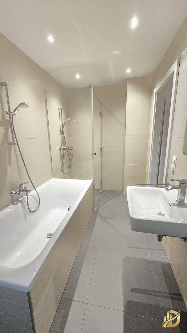 Modernes Badezimmer mit Badewanne, Waschbecken und Duschbereich, in hellen Tönen gehalten.