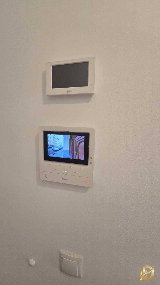 Zwei moderne Gegensprechanlagen mit Bildschirm an einer hellen Wand montiert, für erhöhte Sicherheit.