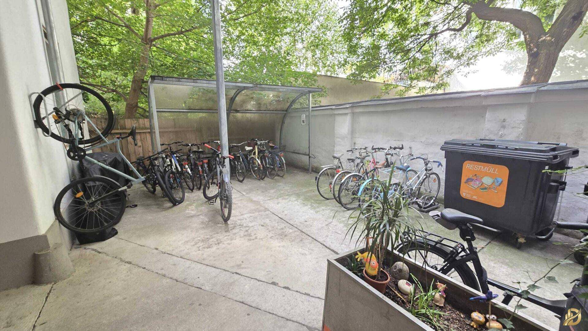 Überdachter Fahrradabstellplatz und Mülltonnen in einem begrünten Außenbereich, gut organisiert und zugänglich.