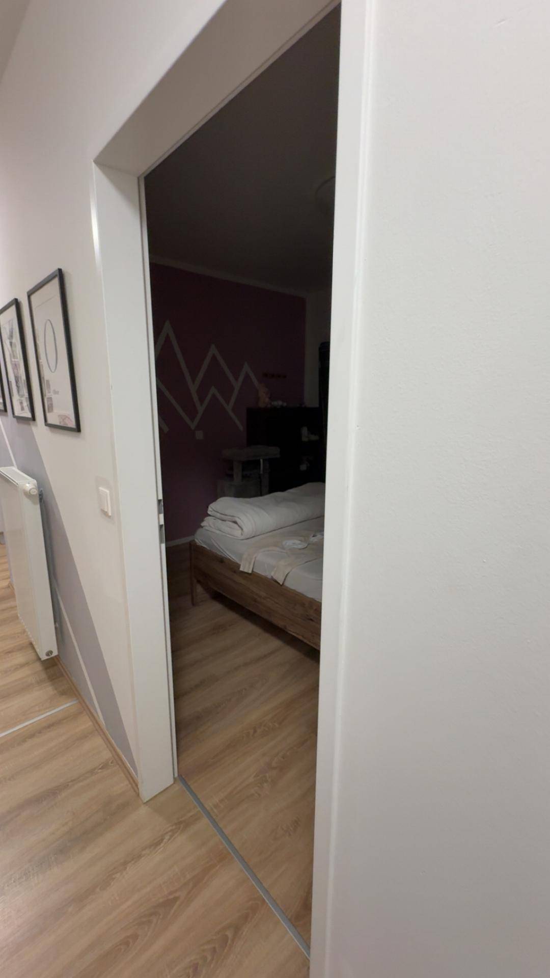 Schlafzimmer mit Bett und farbiger Wandgestaltung, sichtbar durch den Türrahmen.