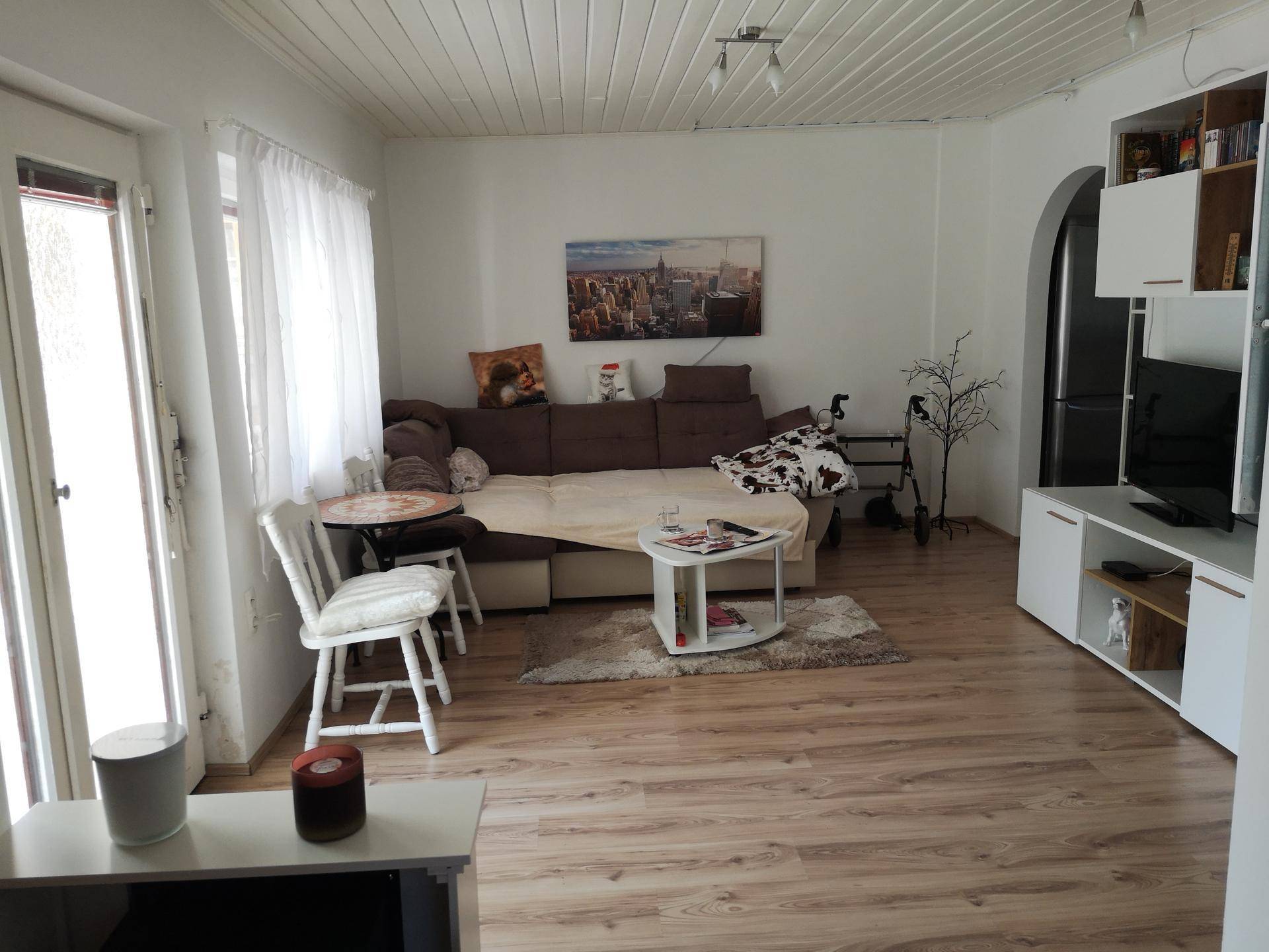 Gemütliches Wohnzimmer mit Sofa, Laminatboden und Zugang zu einem Außenbereich durch die Tür.