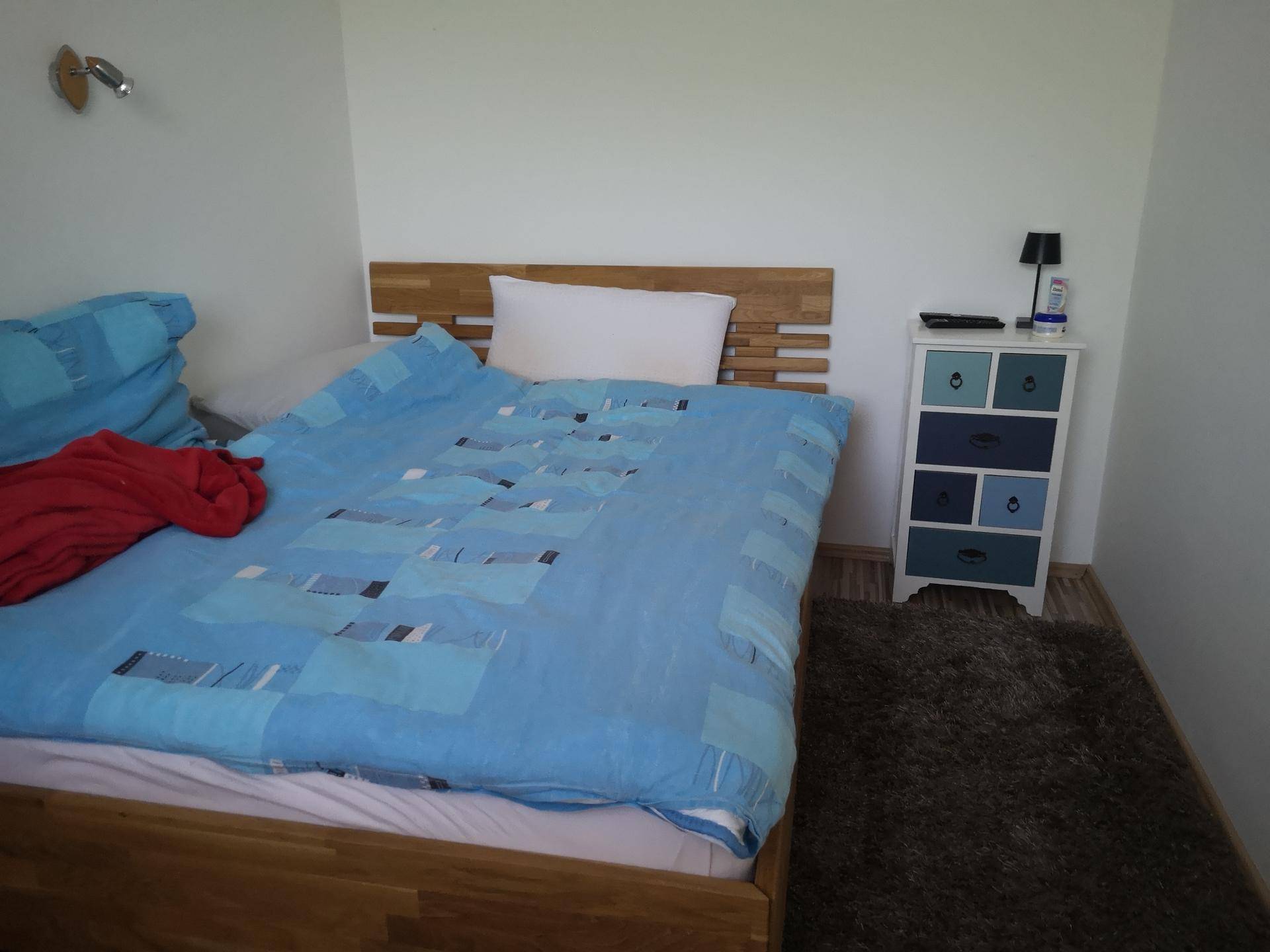 Schlafzimmer mit Holzbett, blauem Bettzeug und einer bunten Kommode auf flauschigem Teppich.