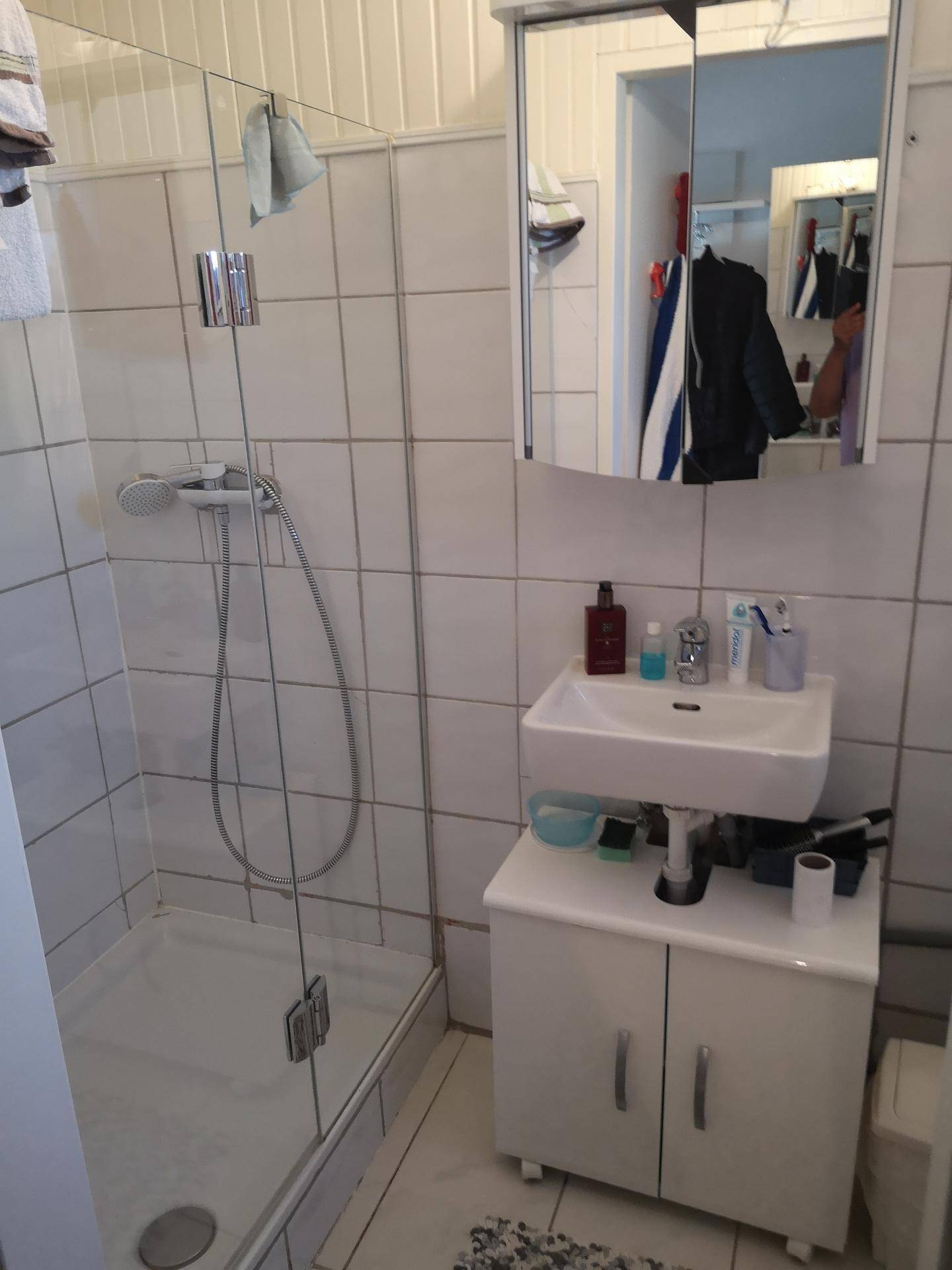 Badezimmer mit Duschkabine, Waschbecken und Spiegelschrank, vollständig gefliest in hellem Design.