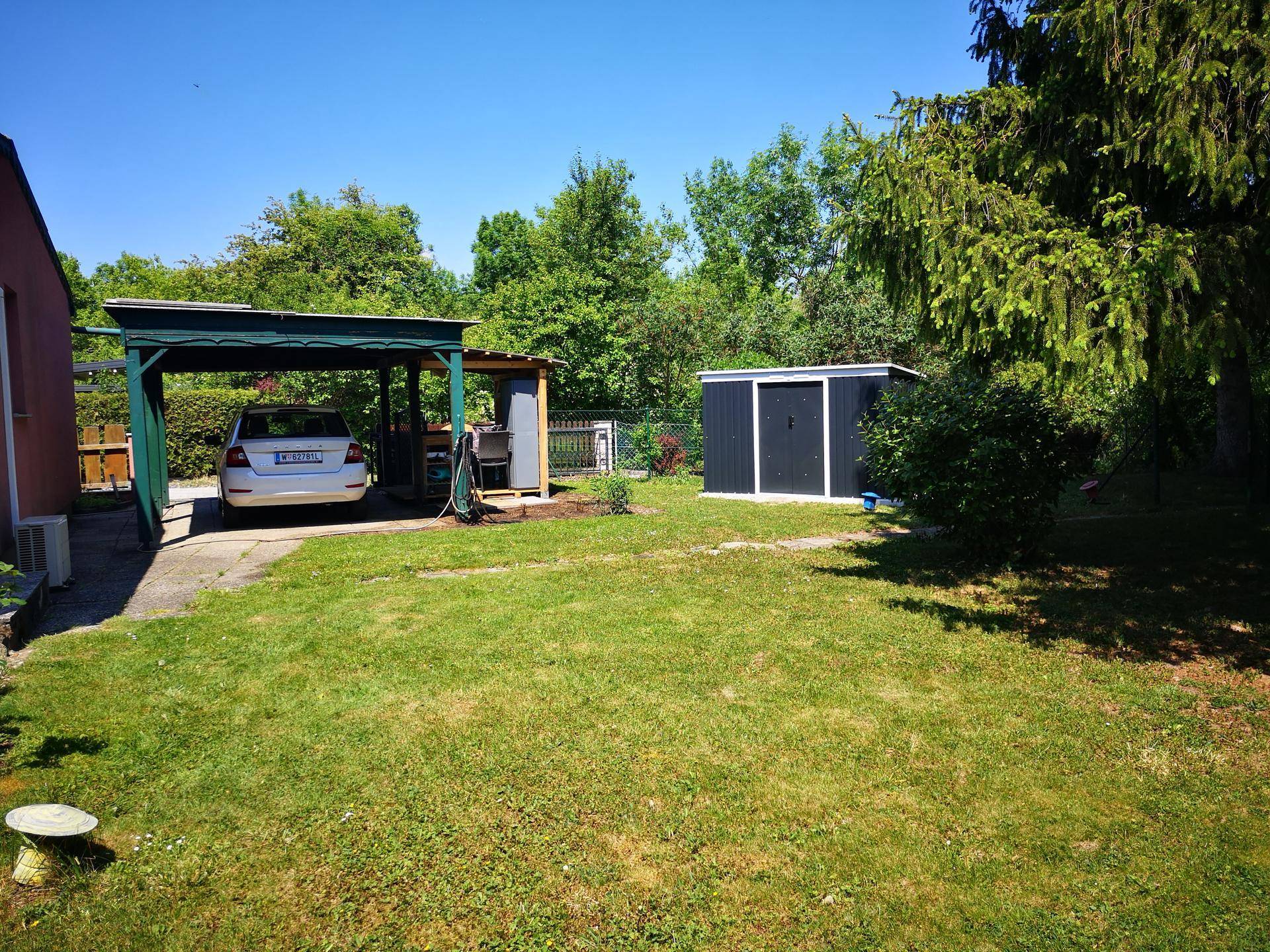 Grüner Garten mit Rasenfläche, einem Carport und einem praktischen Gartenschuppen.