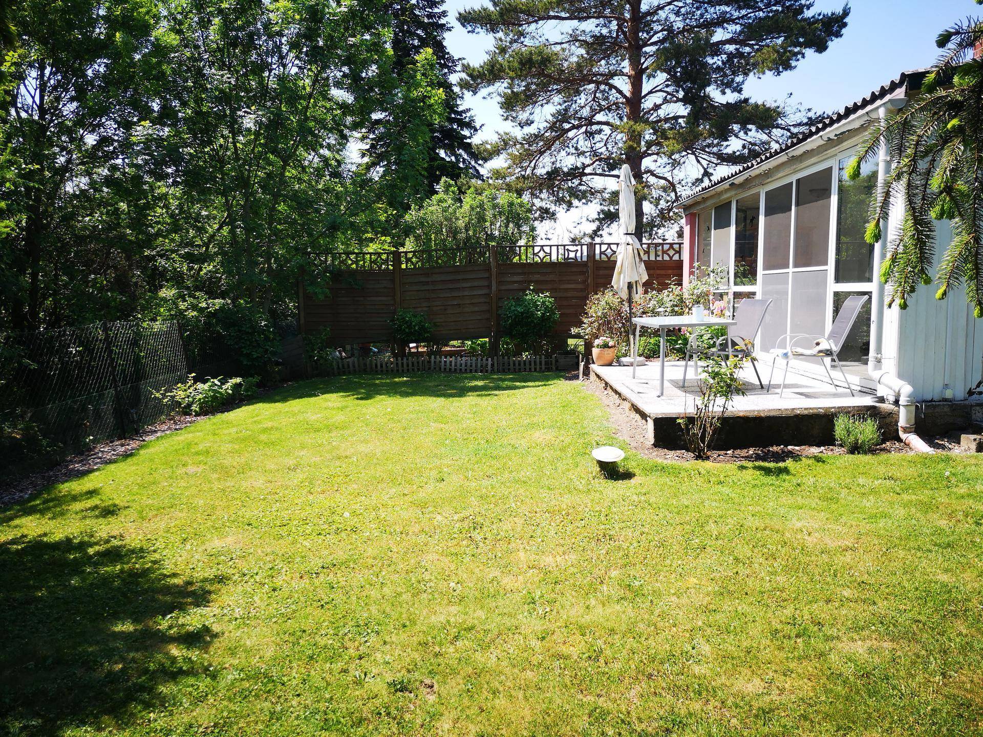 Gepflegter Garten mit Rasenfläche und einer Terrasse mit Gartenmöbeln am Haus.