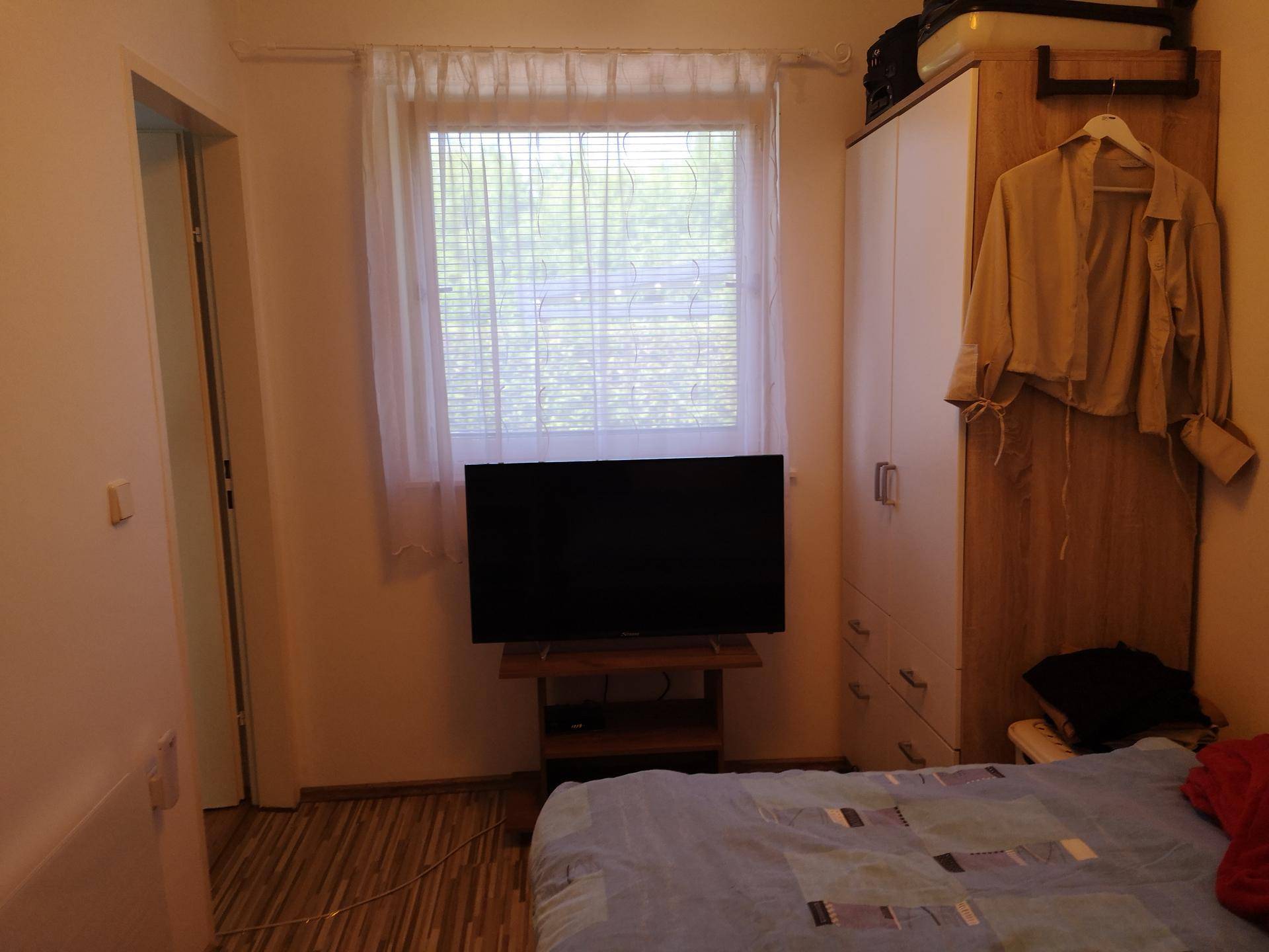 Schlafzimmer mit Bett, Kleiderschrank und Fernseher, ausgestattet mit Laminatboden und Fenster.