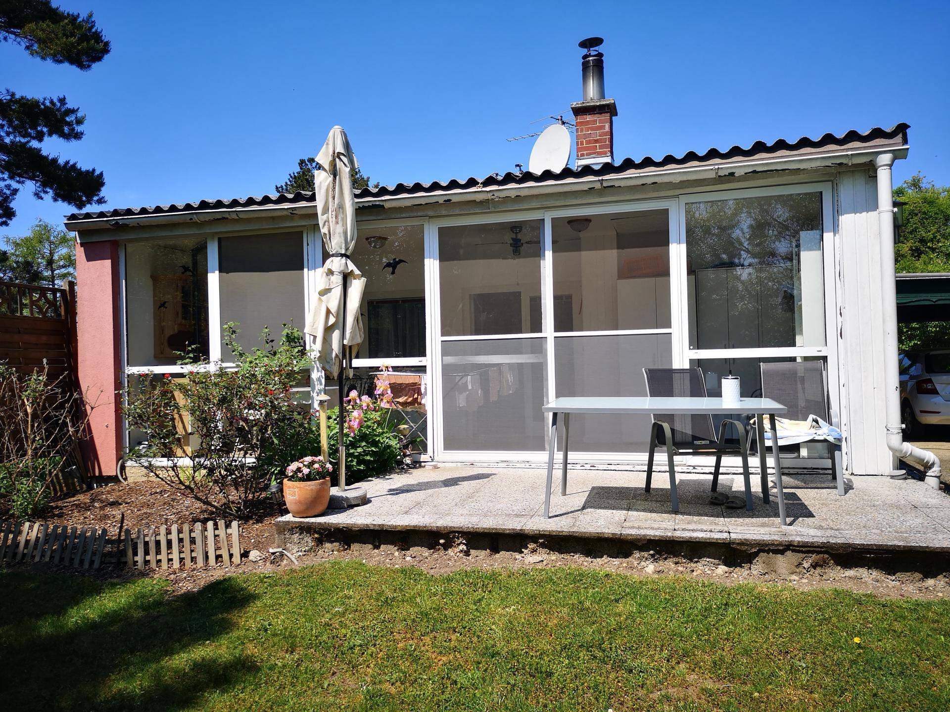 Hausfassade mit großer Terrasse, Gartenmöbeln und weiten Fensterfronten zum Garten hin.