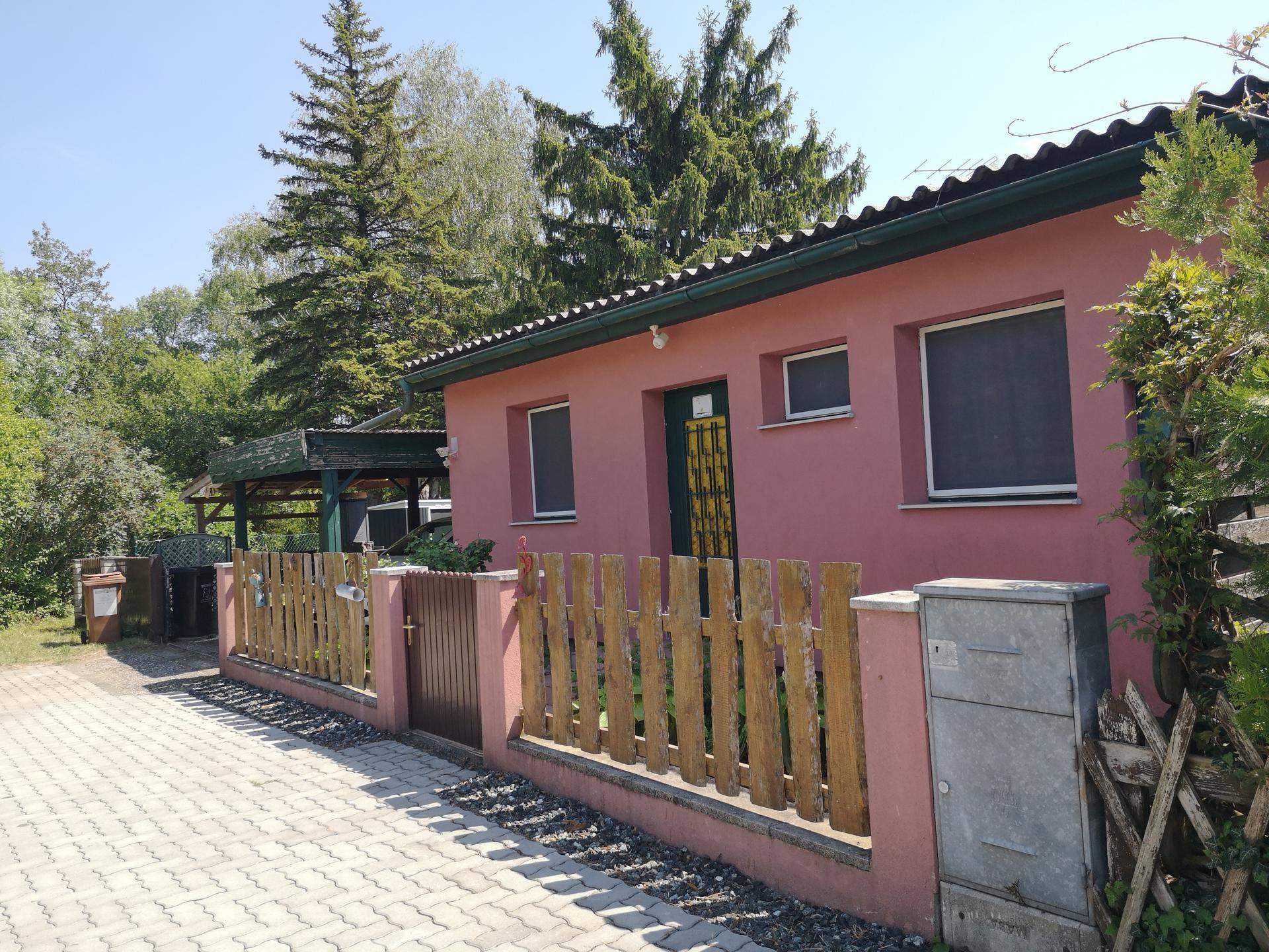 Vorderansicht des Hauses mit Zaun, gepflasterter Auffahrt und Carport im Hintergrund.