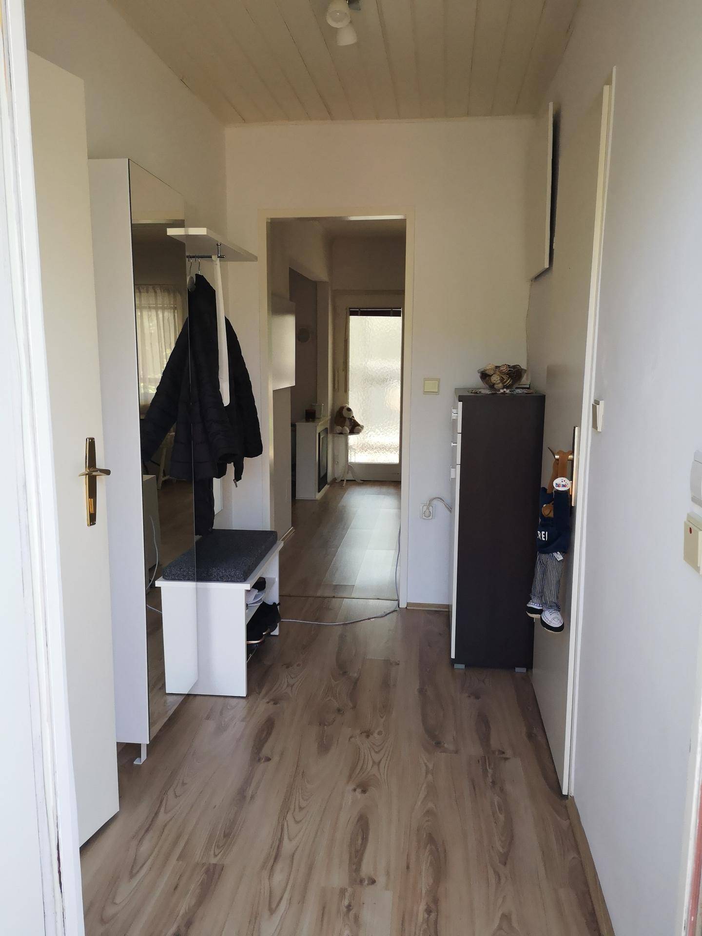 Heller Flur mit Laminatboden, Garderobe und Spiegel, der zu weiteren Räumen führt.