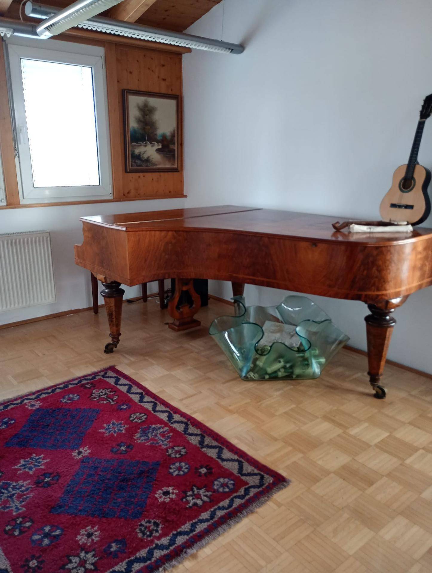 Heller Wohnraum mit einem eleganten Flügel, Gitarre und Holzbalkendecke unter einer Dachschräge.