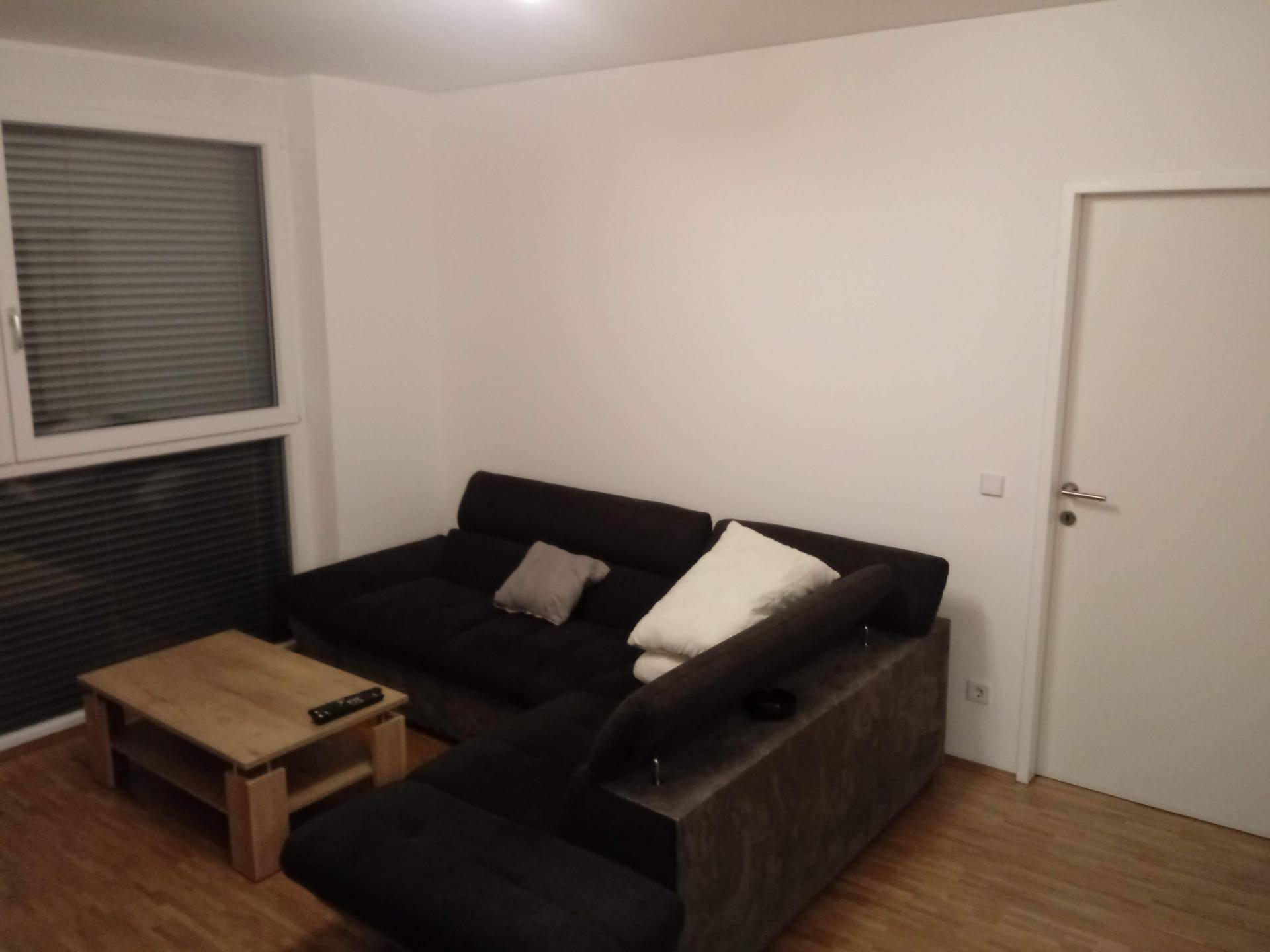 Gemütliches Wohnzimmer mit Ecksofa, Couchtisch und Fenster mit Jalousien.
