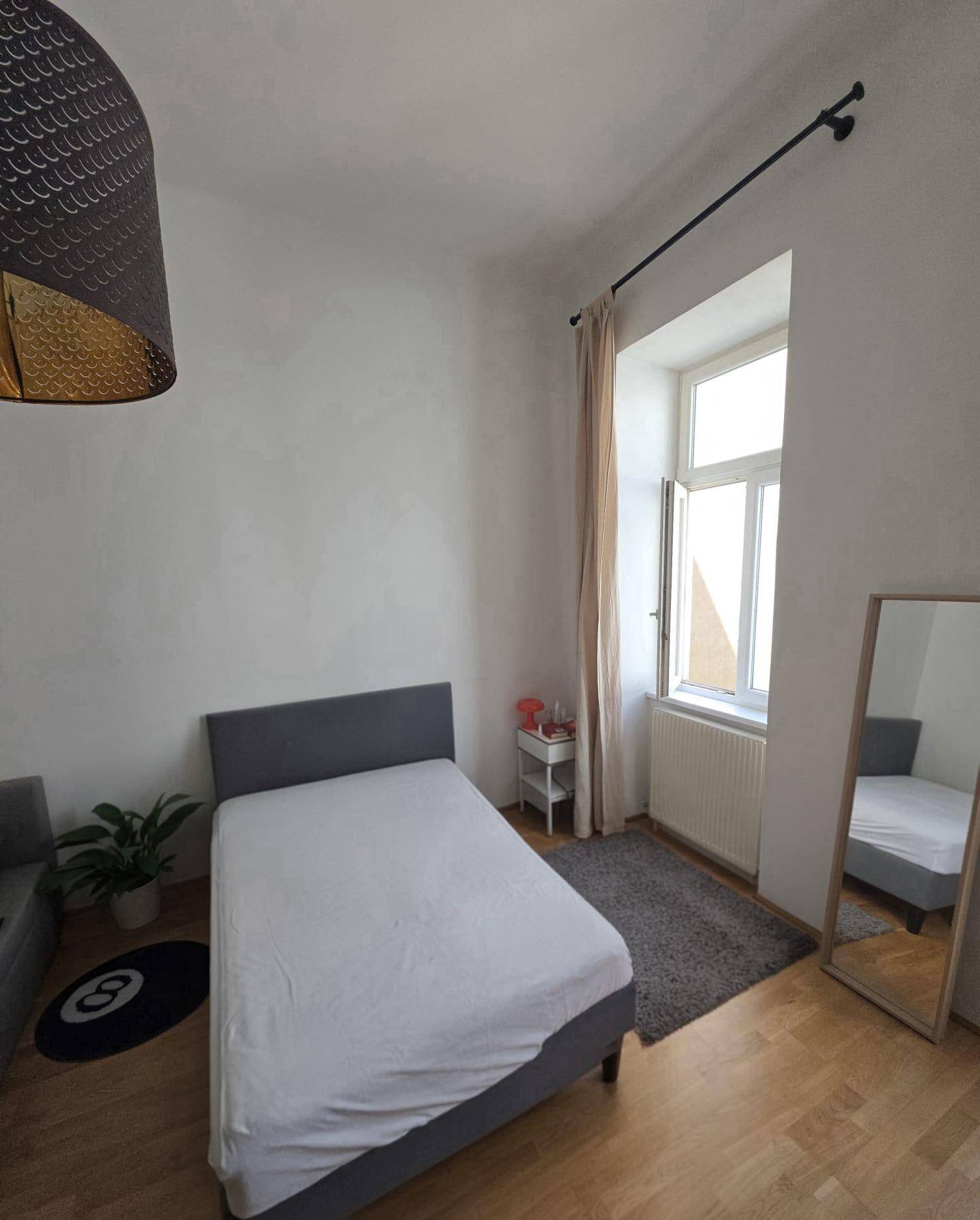 Schlafzimmer mit Einzelbett, Fenster und dekorativer Hängelampe.