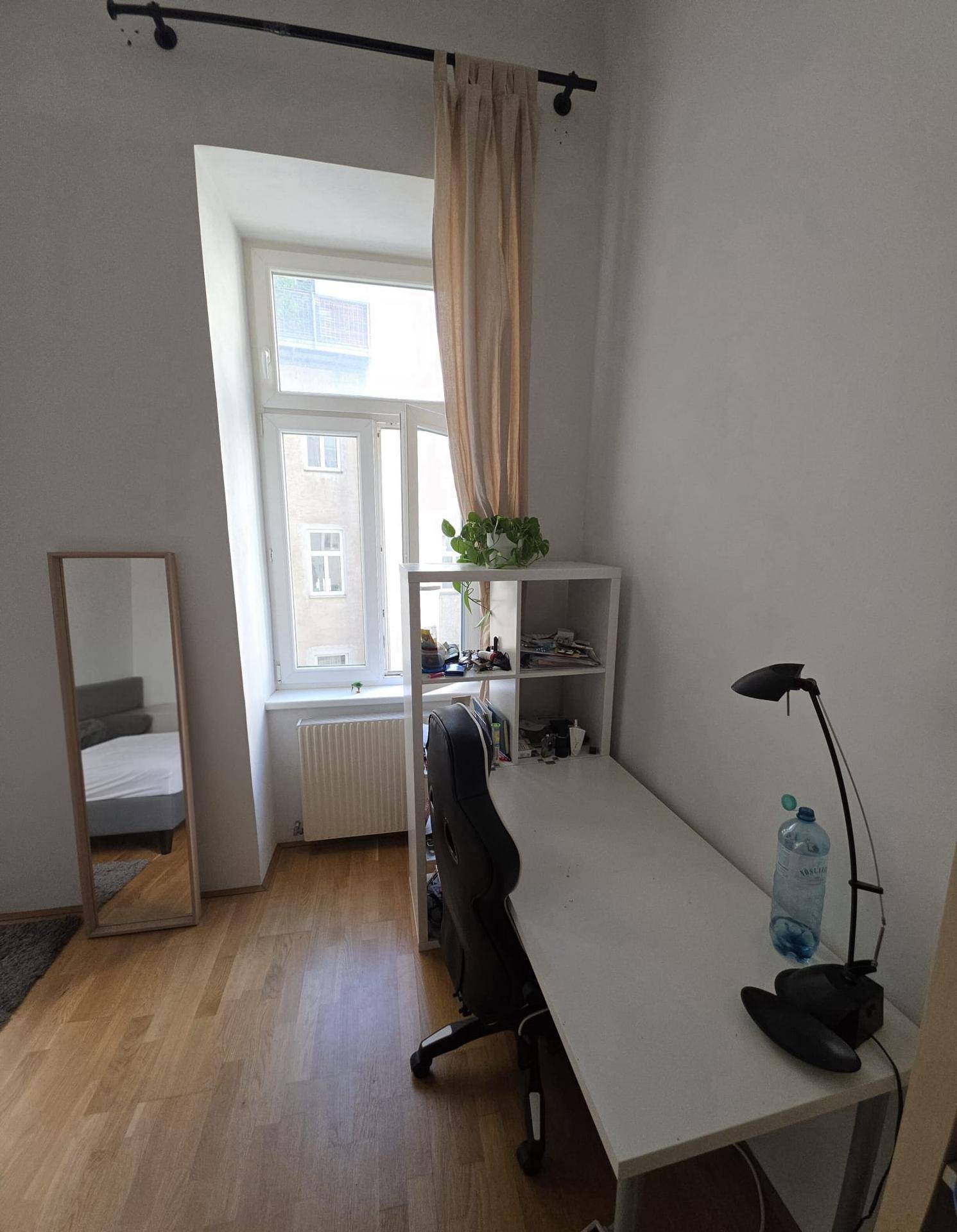 Arbeitsbereich im Schlafzimmer mit Schreibtisch, Regal und Fenster.