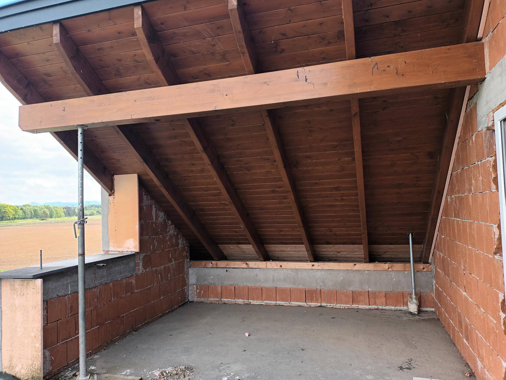 Unfertiger Balkonbereich mit sichtbaren Holzbalken und Ziegelwänden, bereit für den Ausbau.