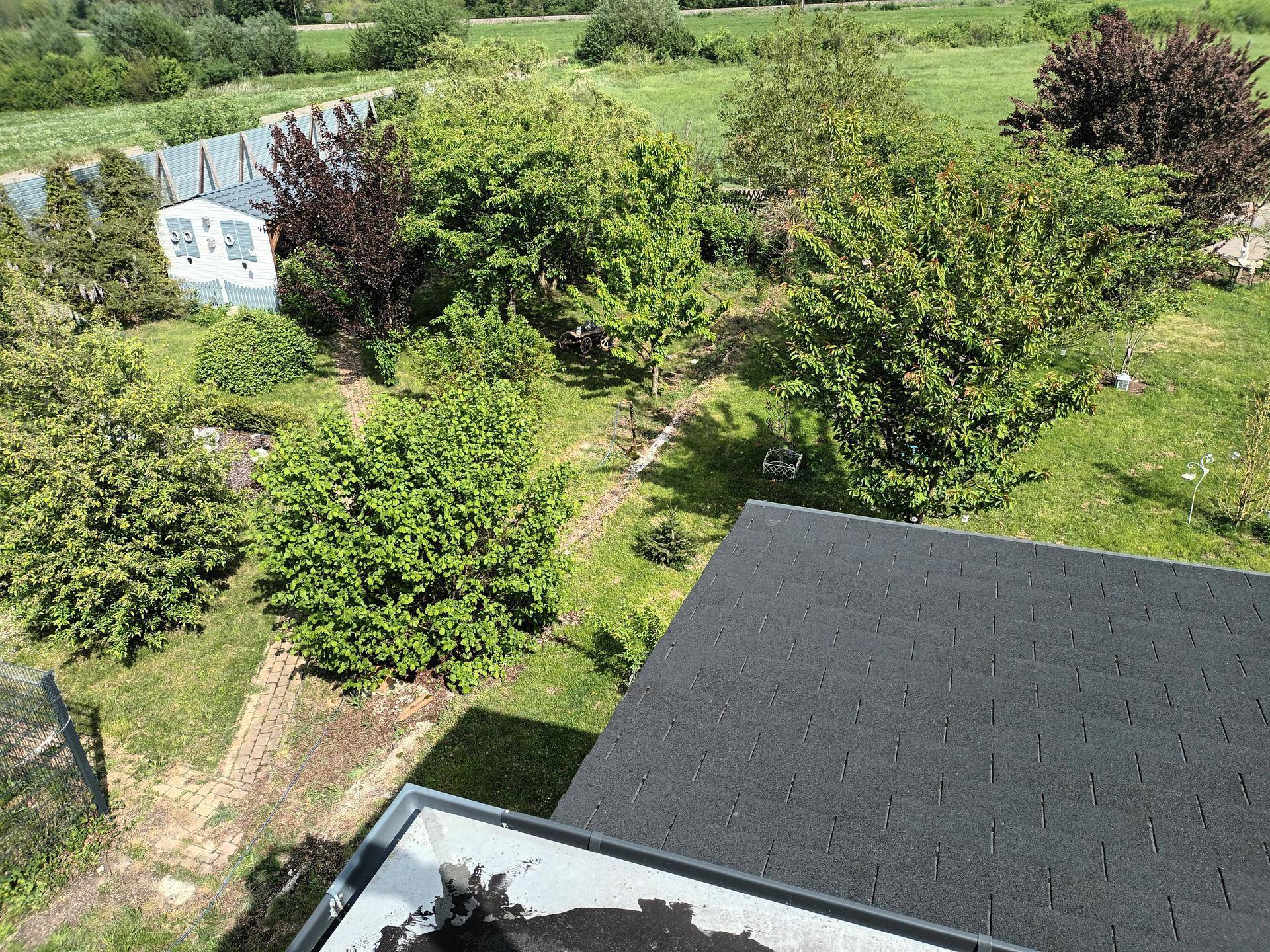 Vogelperspektive des weitläufigen Gartens mit Bäumen, Wegen und angrenzenden Feldern unter blauem Himmel.