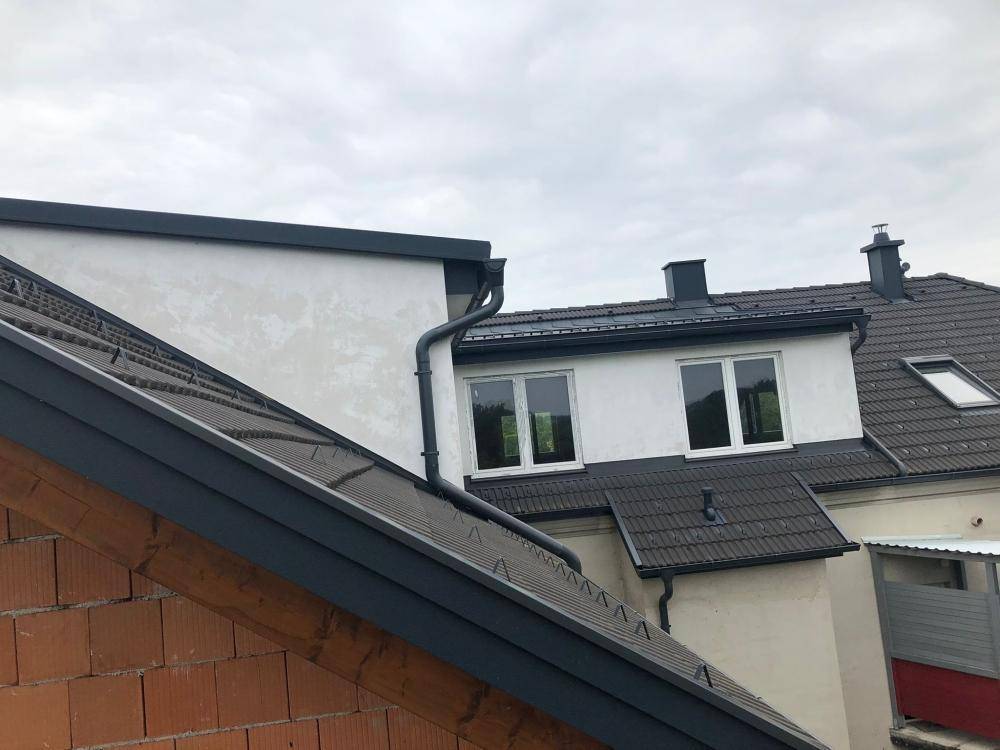 Detailansicht des Daches mit dunklen Dachziegeln und weißen Gaubenfenstern an der Fassade.