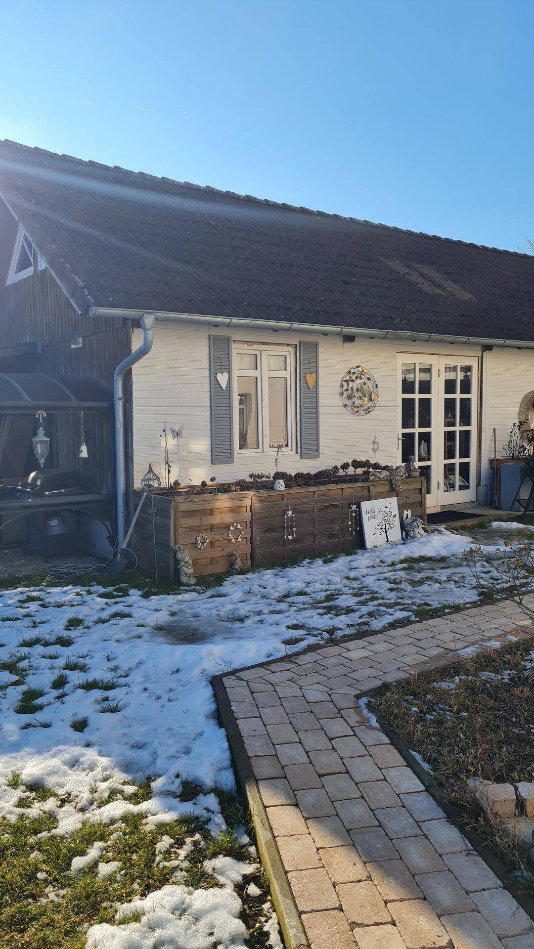 Kleineres Gebäude im Garten mit verschneitem Rasen, gepflastertem Weg und dekorativen Elementen.