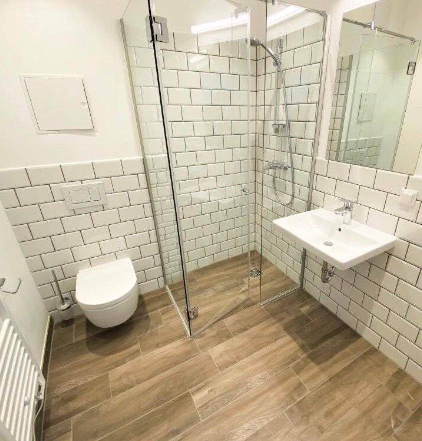 Modernes Badezimmer mit weißen Metrofliesen, bodengleicher Dusche und wandhängendem WC.