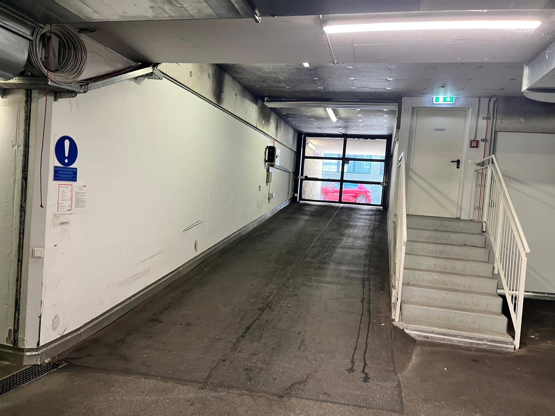Einfahrt zur Tiefgarage mit Rampe, Treppenhaus und Sicherheitshinweisen.