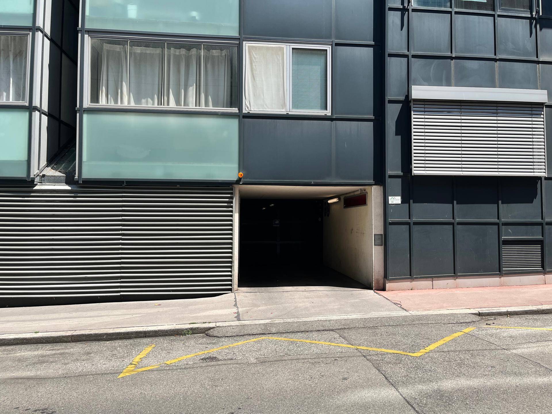 Moderne Gebäudefassade mit Tiefgarageneinfahrt und großen Fenstern.