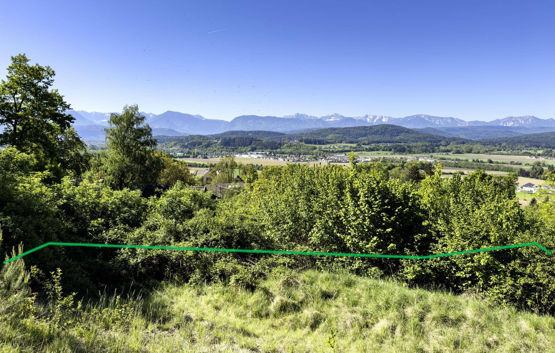 Panoramablick über grüne Hügel und ferne Berge, mit einer grünen Linie, die ein Grundstück markiert.