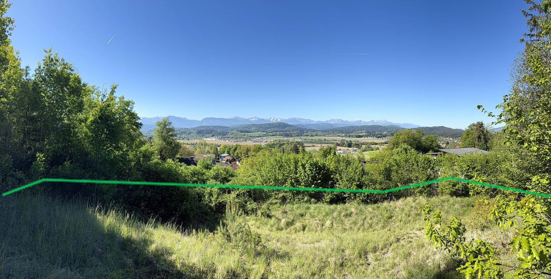 Weitläufiger Landschaftsblick mit grünen Bäumen, Hügeln und einer Bergkette am Horizont, markiert mit einer grünen Linie.
