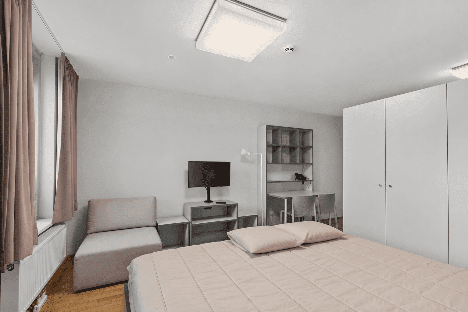 Gemütliches Studio-Apartment mit Bett, Kleiderschrank und Schreibtischbereich.