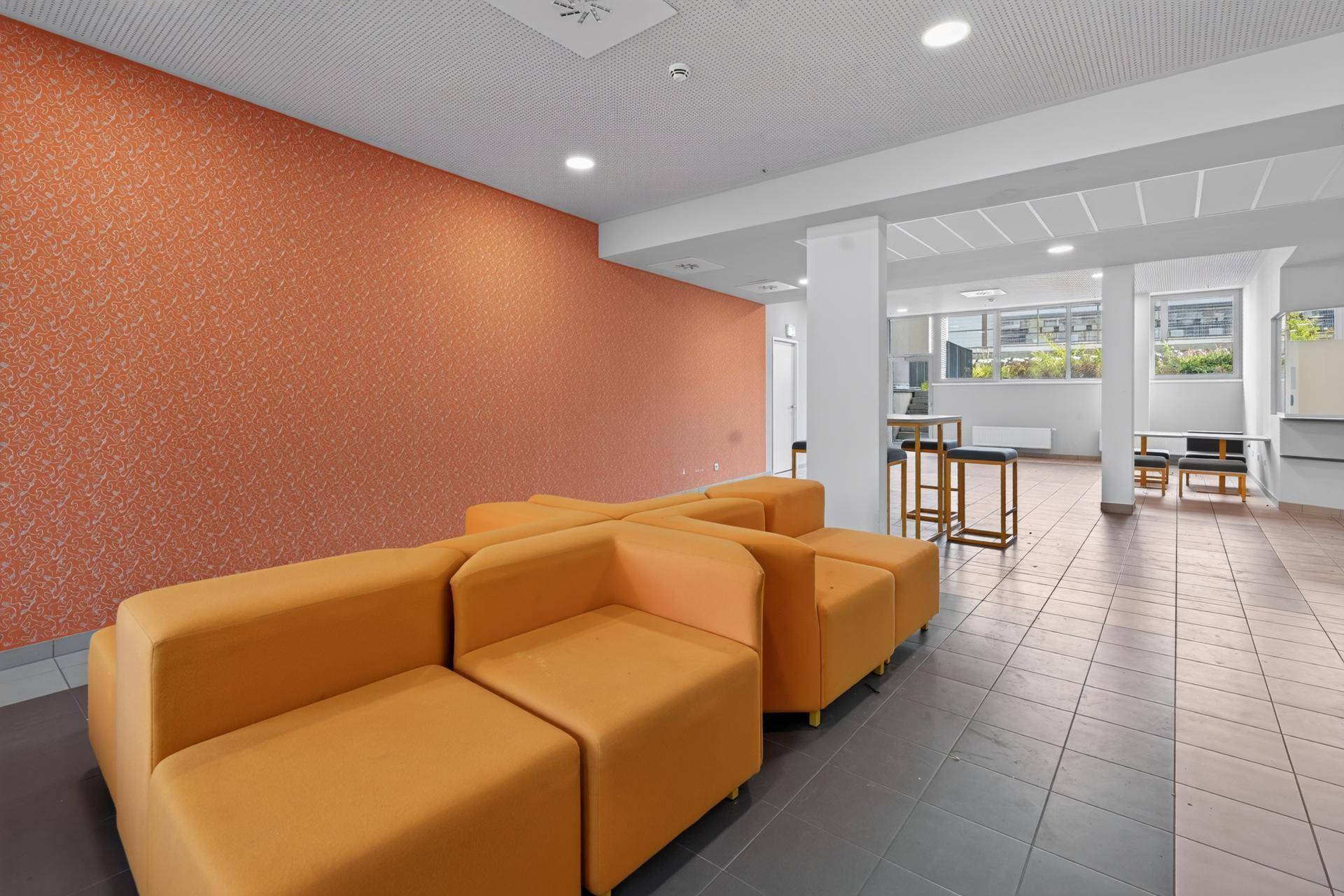 Gemeinschaftsraum mit orangefarbenen Sitzgelegenheiten und Fliesenboden.