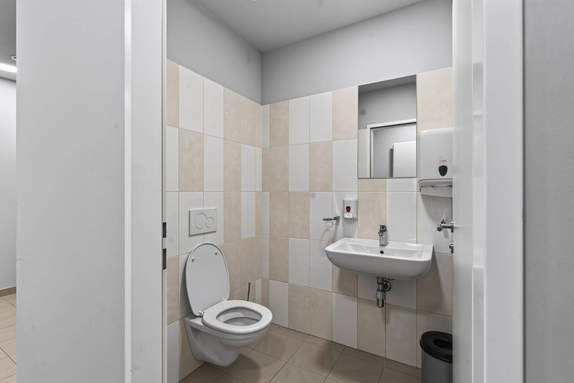 Funktionale Toilette mit Fliesen an den Wänden und einem kleinen Waschbecken.