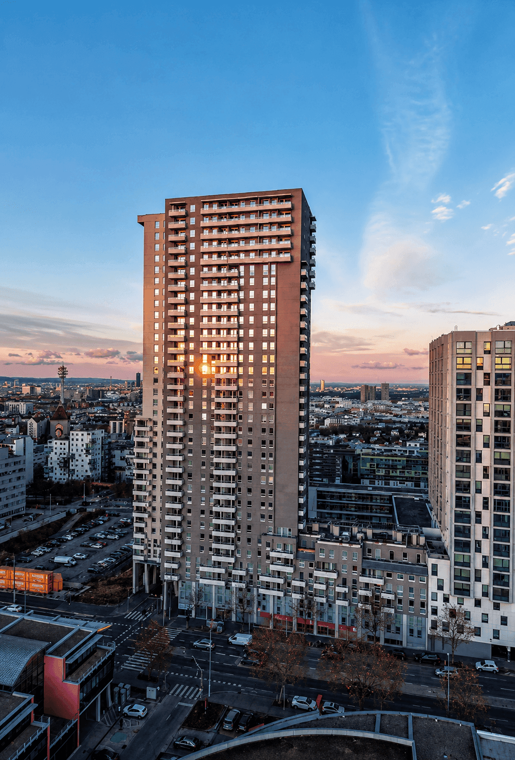 Hohes Wohngebäude bei Sonnenuntergang mit Stadtblick und vielen Fenstern.