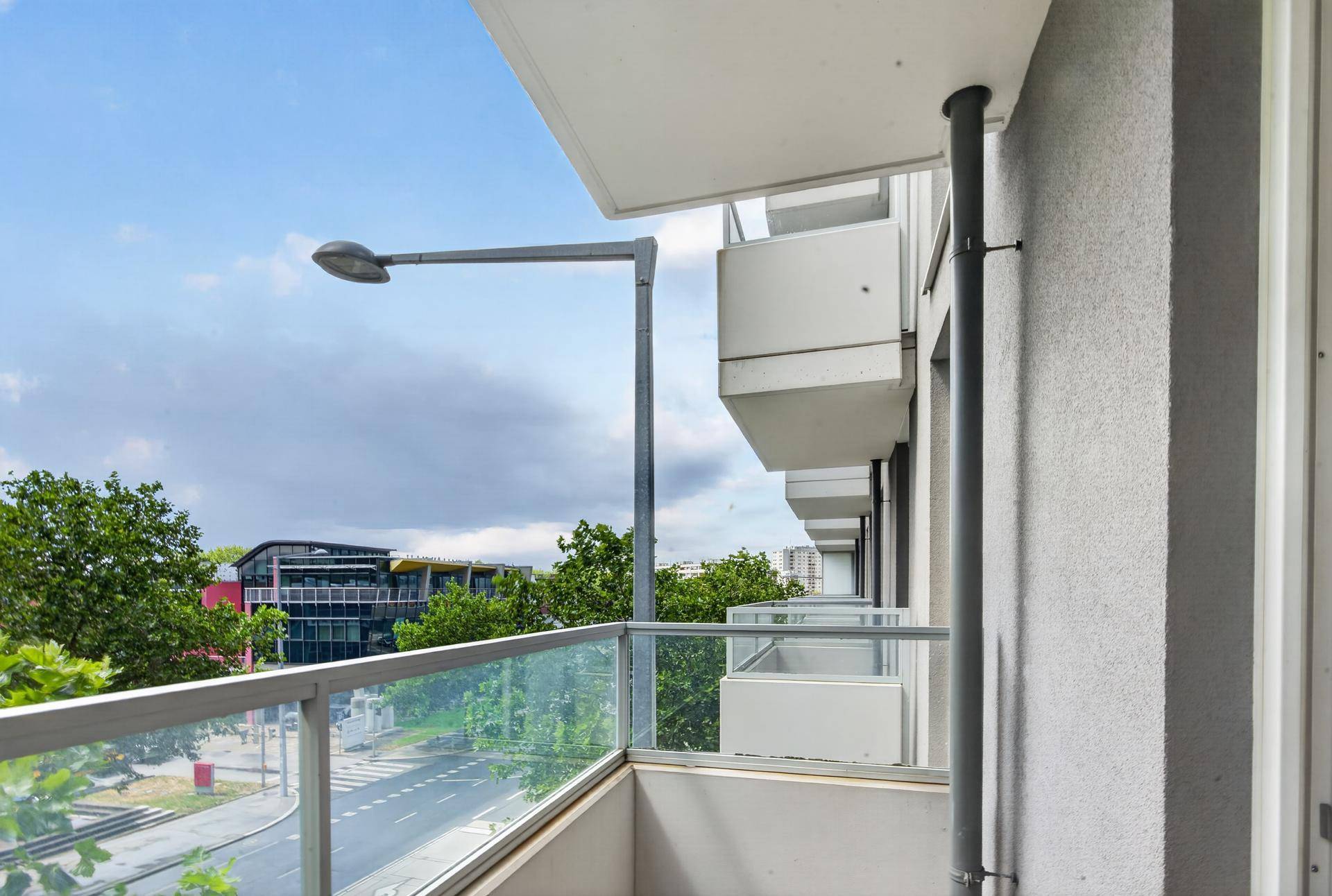 Balkon mit Glasgeländer und Blick auf die Straße und Bäume.