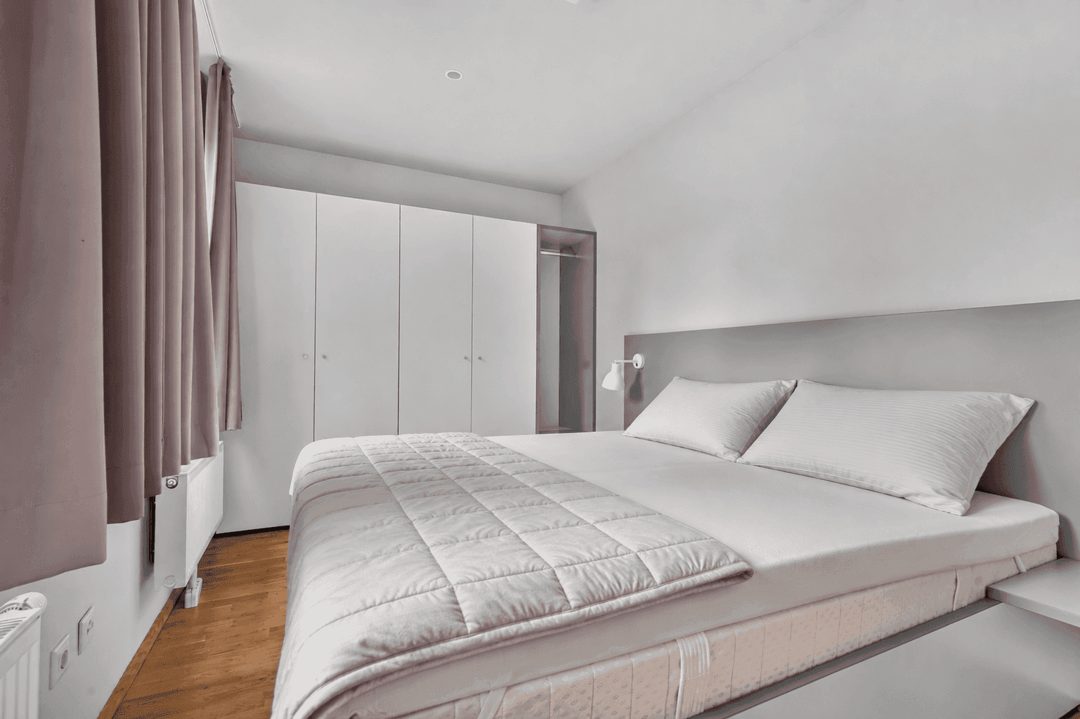 Schlafzimmer mit Doppelbett, Einbauschränken und Holzboden.