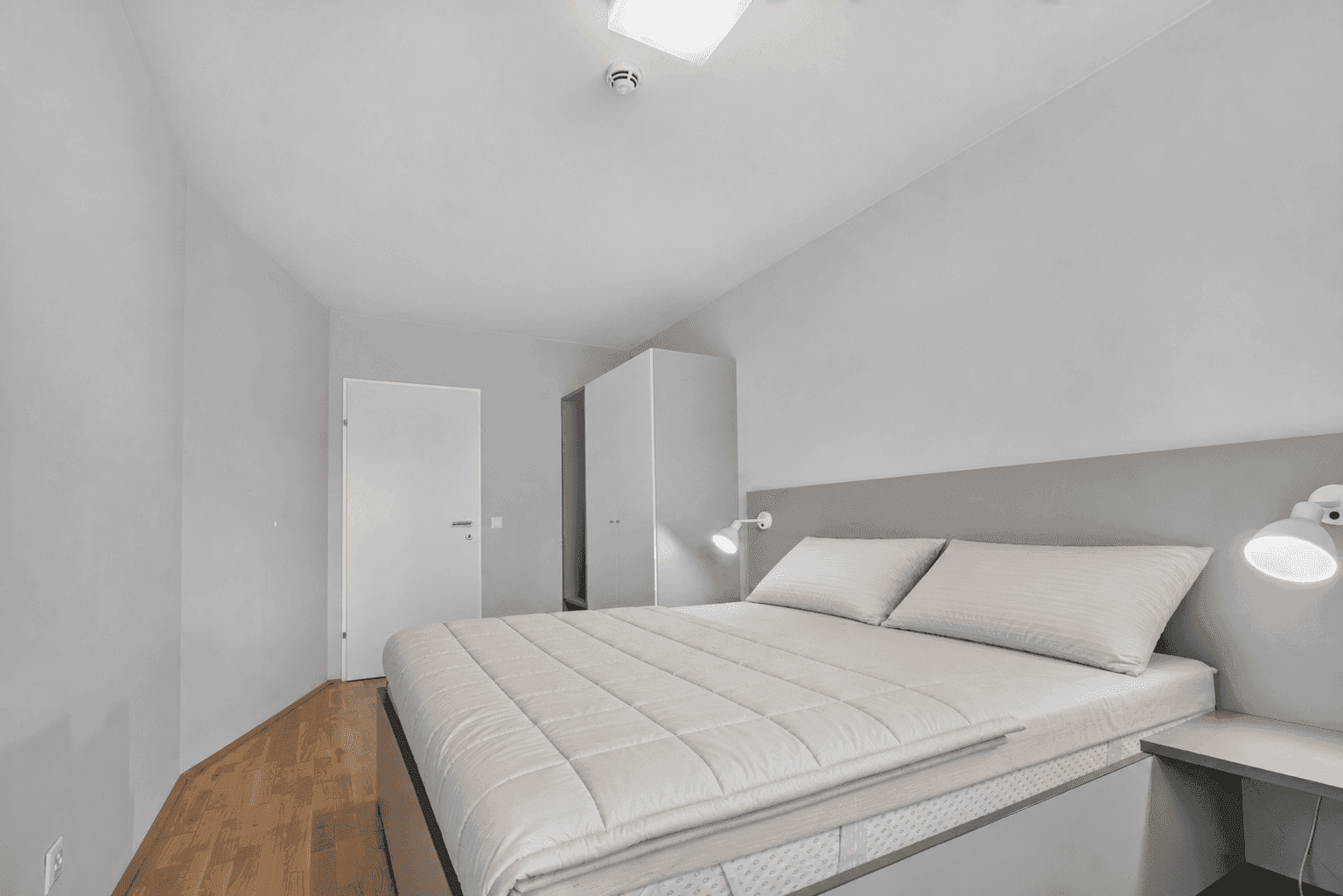 Helles Schlafzimmer mit Doppelbett, Nachttischen und Holzboden.