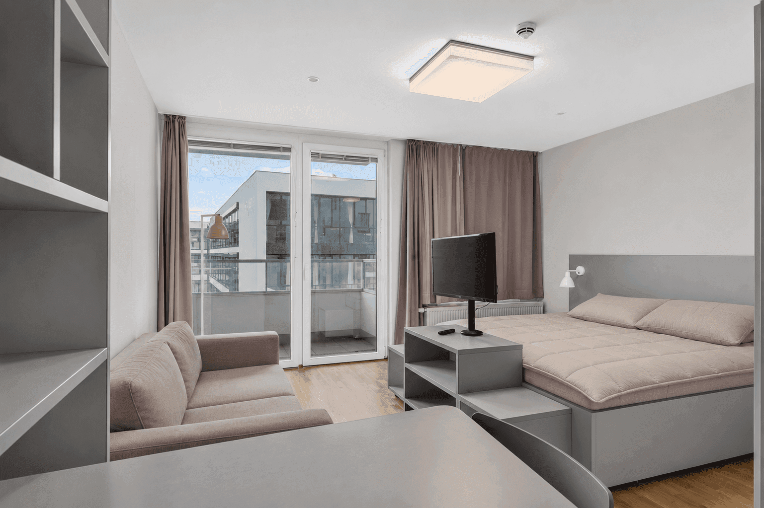 Modernes Studio-Apartment mit Balkonzugang, Bett, Sofa und Schreibtisch.