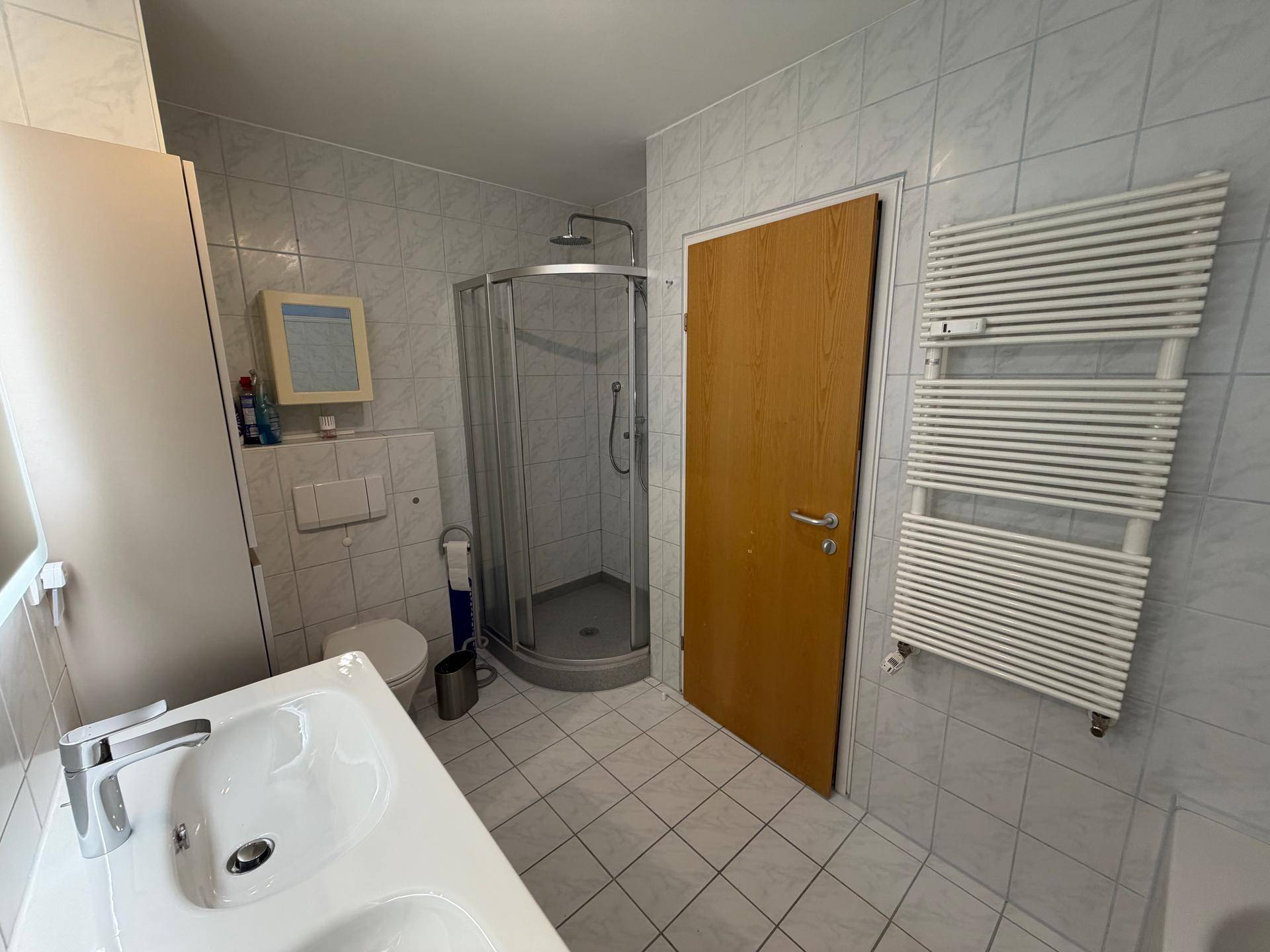 Helles Badezimmer mit Duschkabine, Waschbecken, Toilette und beheiztem Handtuchhalter.