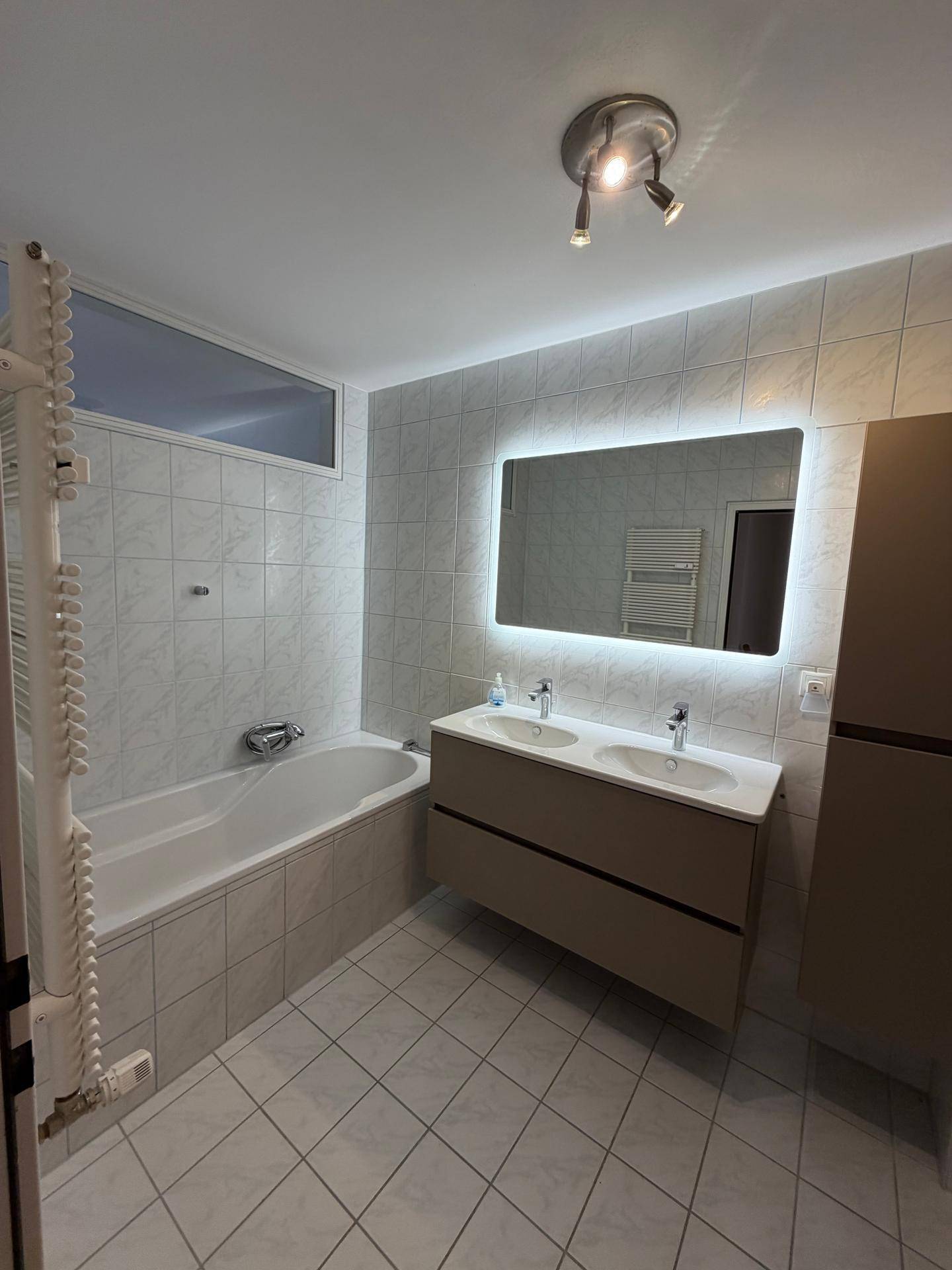 Modernes Badezimmer mit Badewanne, Doppelwaschbecken und beleuchtetem Spiegelschrank.