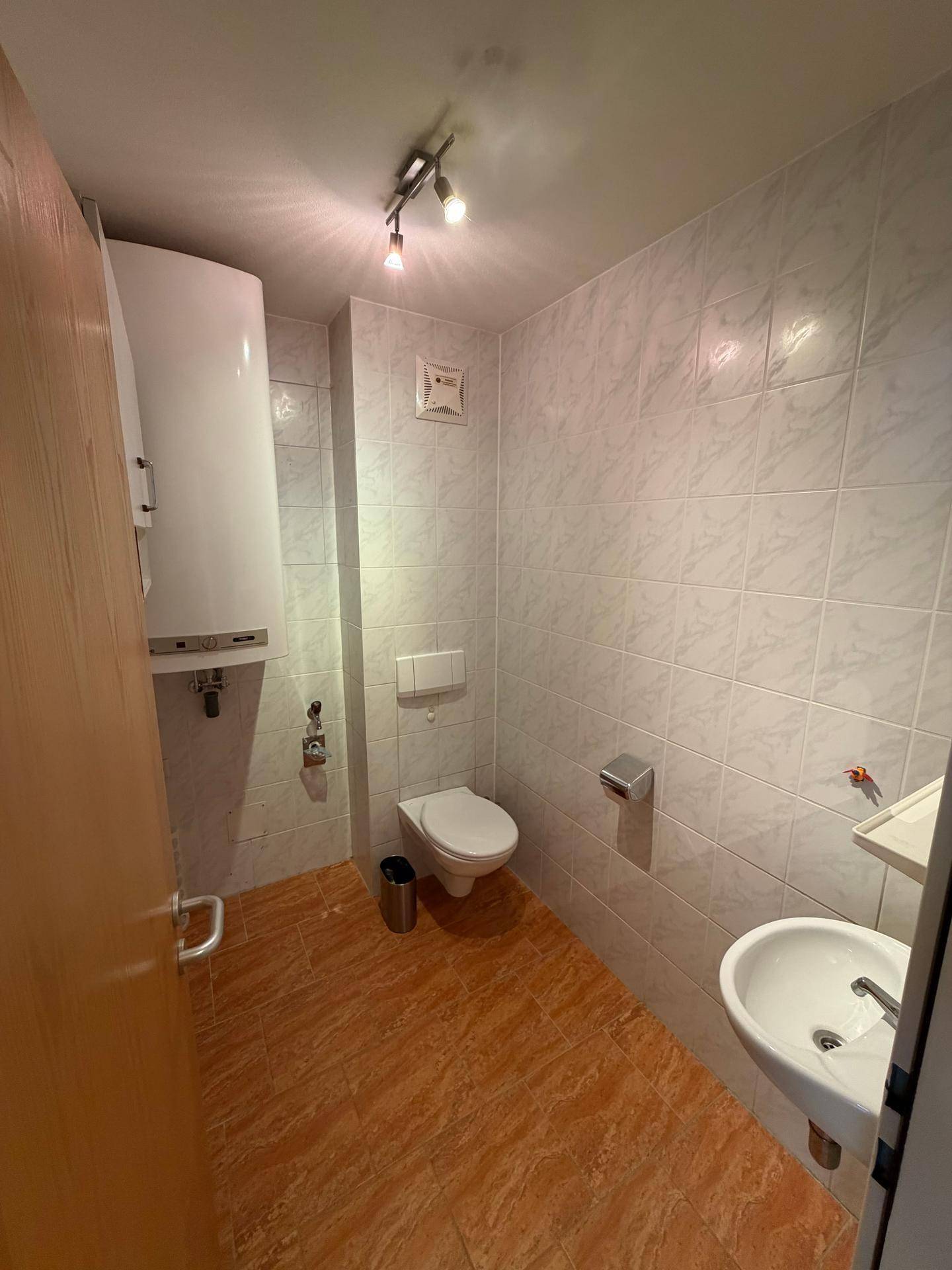 Kleines Gäste-WC mit gefliesten Wänden, Toilette, Waschbecken und Warmwasserboiler.