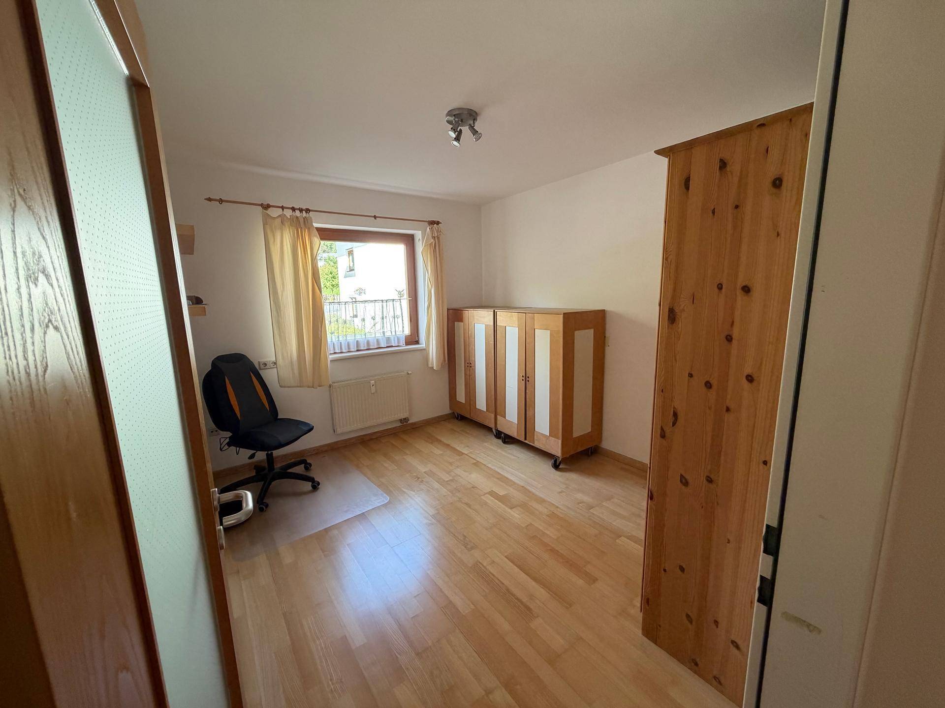Helles Schlafzimmer oder Büro mit Holzfußboden, Fenster und praktischen Holzschränken.