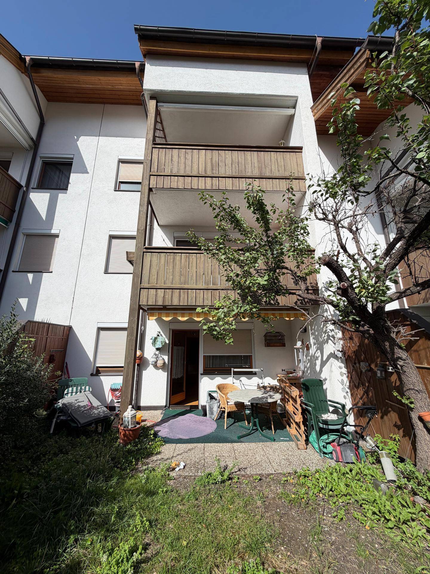 Außenansicht des Gebäudes mit einer möblierten Terrasse im Erdgeschoss und einem Balkon darüber.