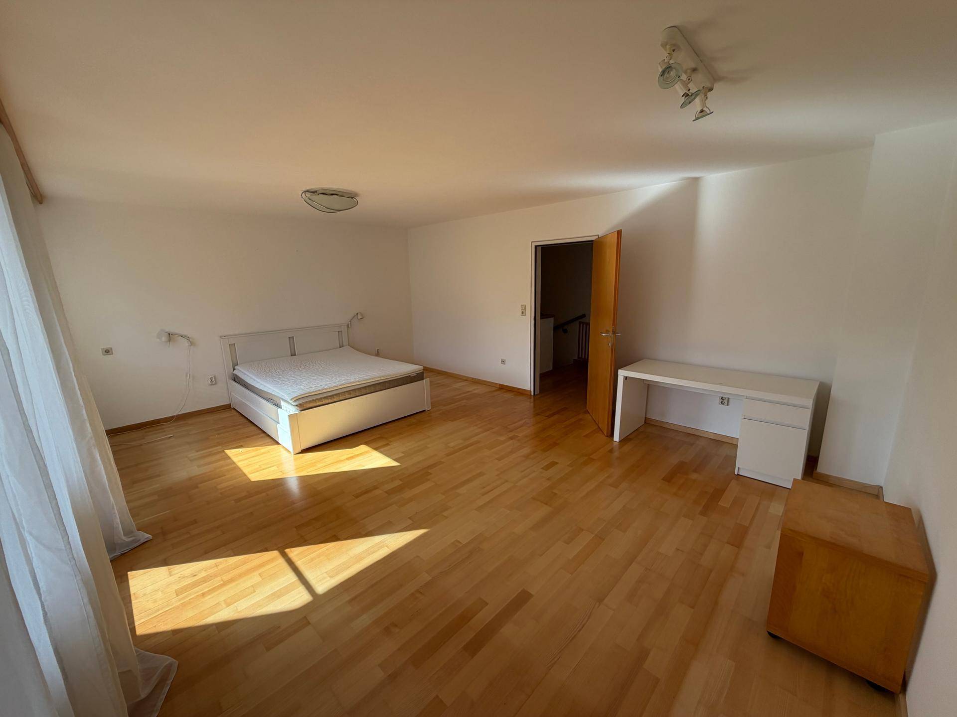 Großes, sonniges Schlafzimmer mit Doppelbett, Schreibtisch und hellem Holzfußboden.