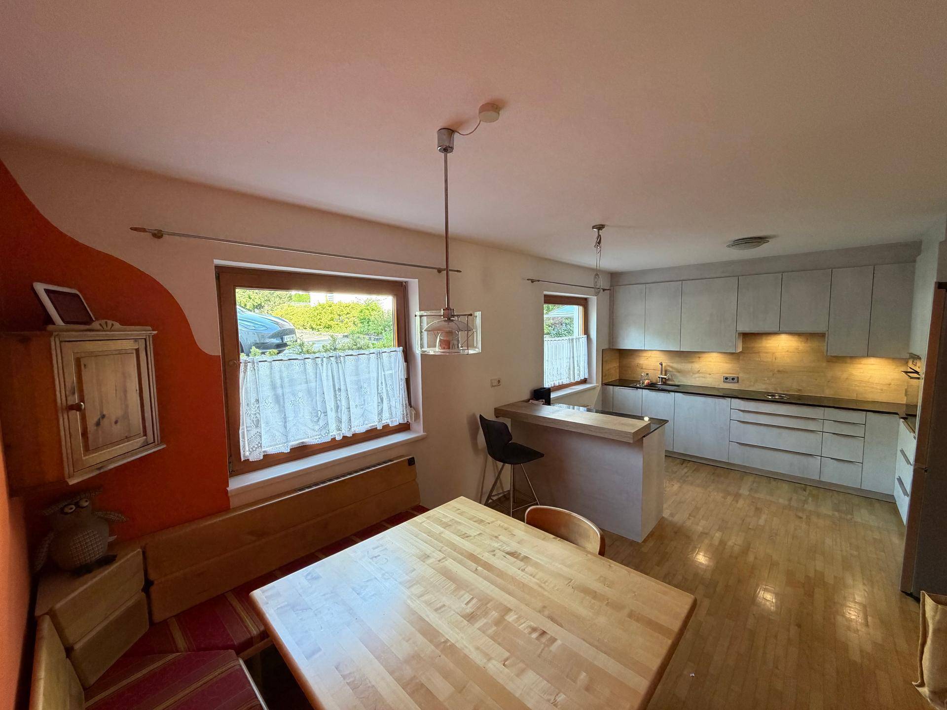 Helle Wohnküche mit Essbereich, Holztisch und modernen hellgrauen Küchenschränken.