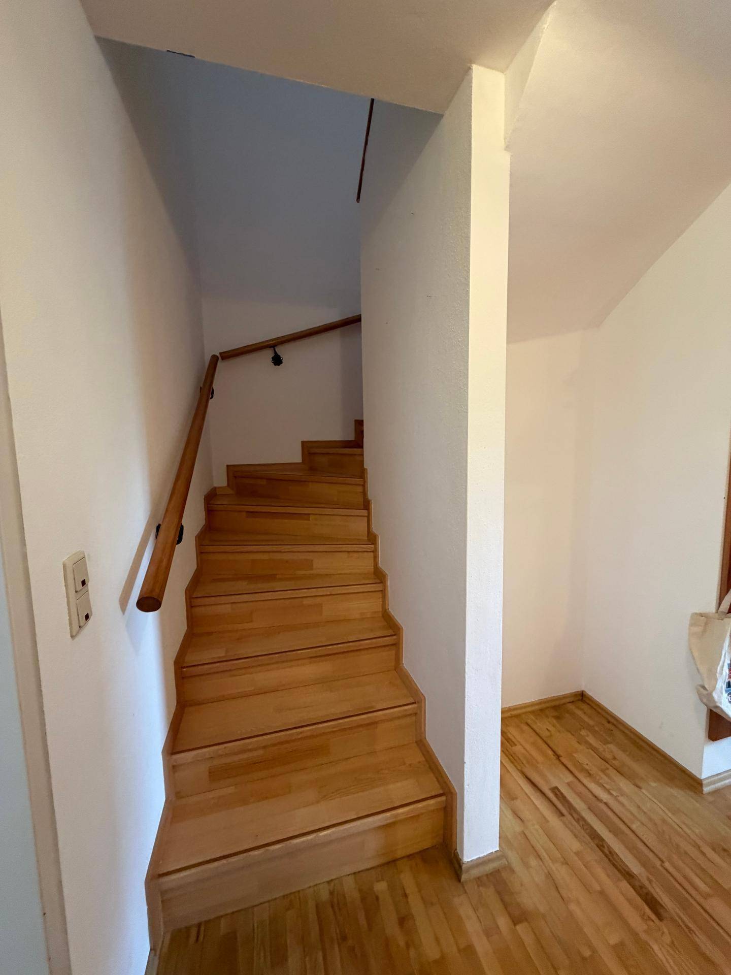 Helle Holztreppe mit Handlauf, die in die obere Etage des Hauses führt.