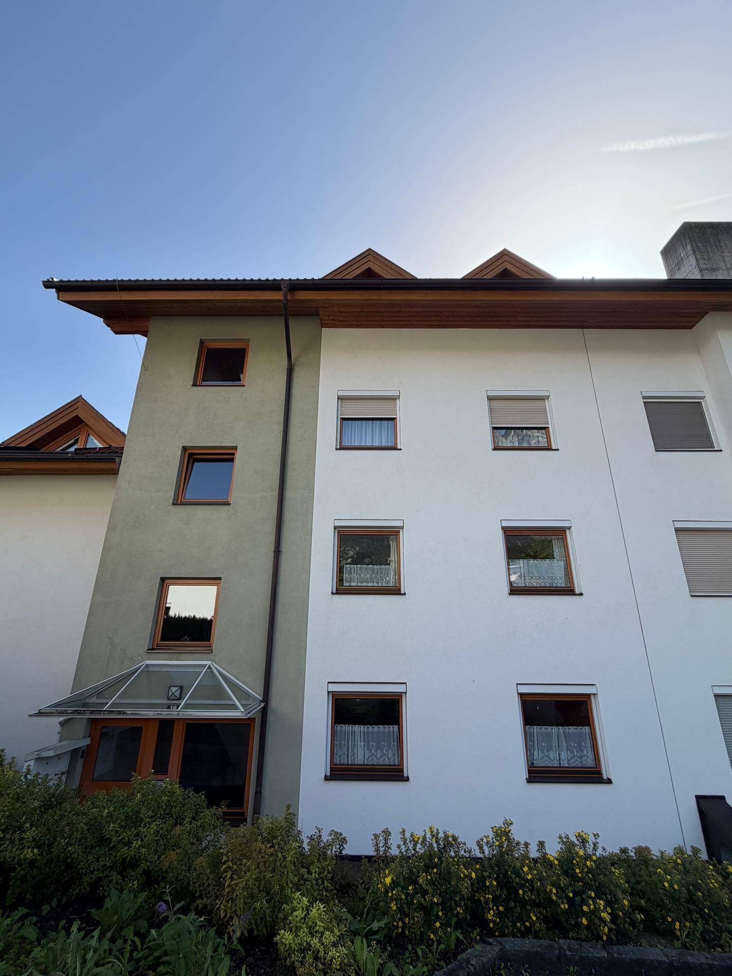 Fassade eines Wohnhauses mit mehreren Fenstern und einem Eingangsbereich mit Glasüberdachung.