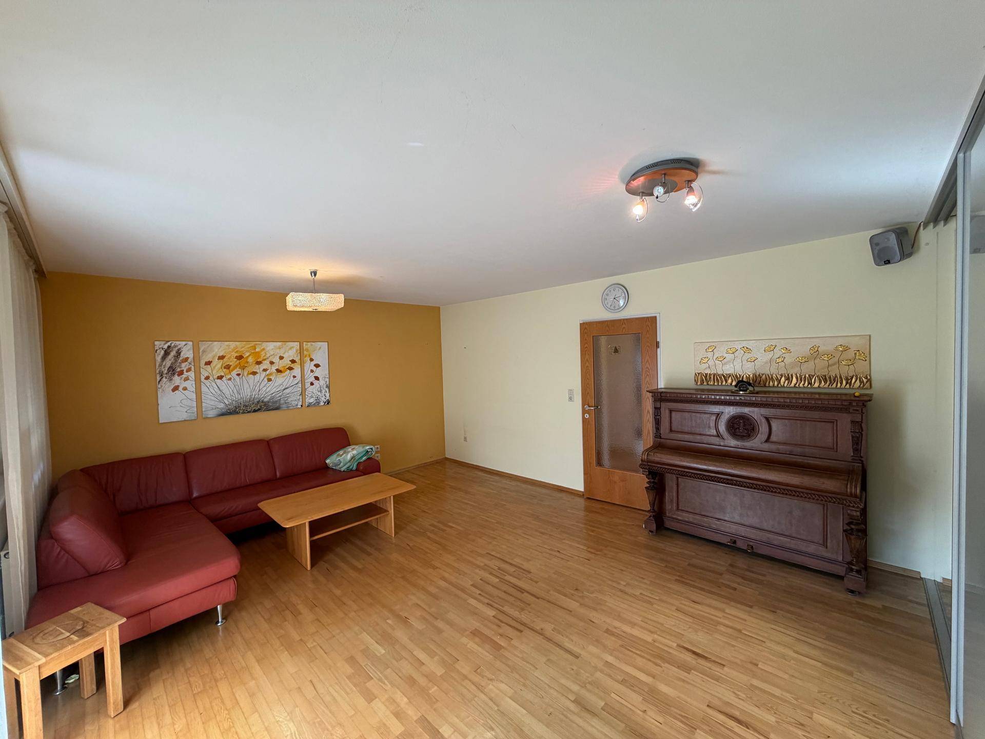 Geräumiges Wohnzimmer mit Holzboden, roter Eckcouch und dekorativen Wandbildern.