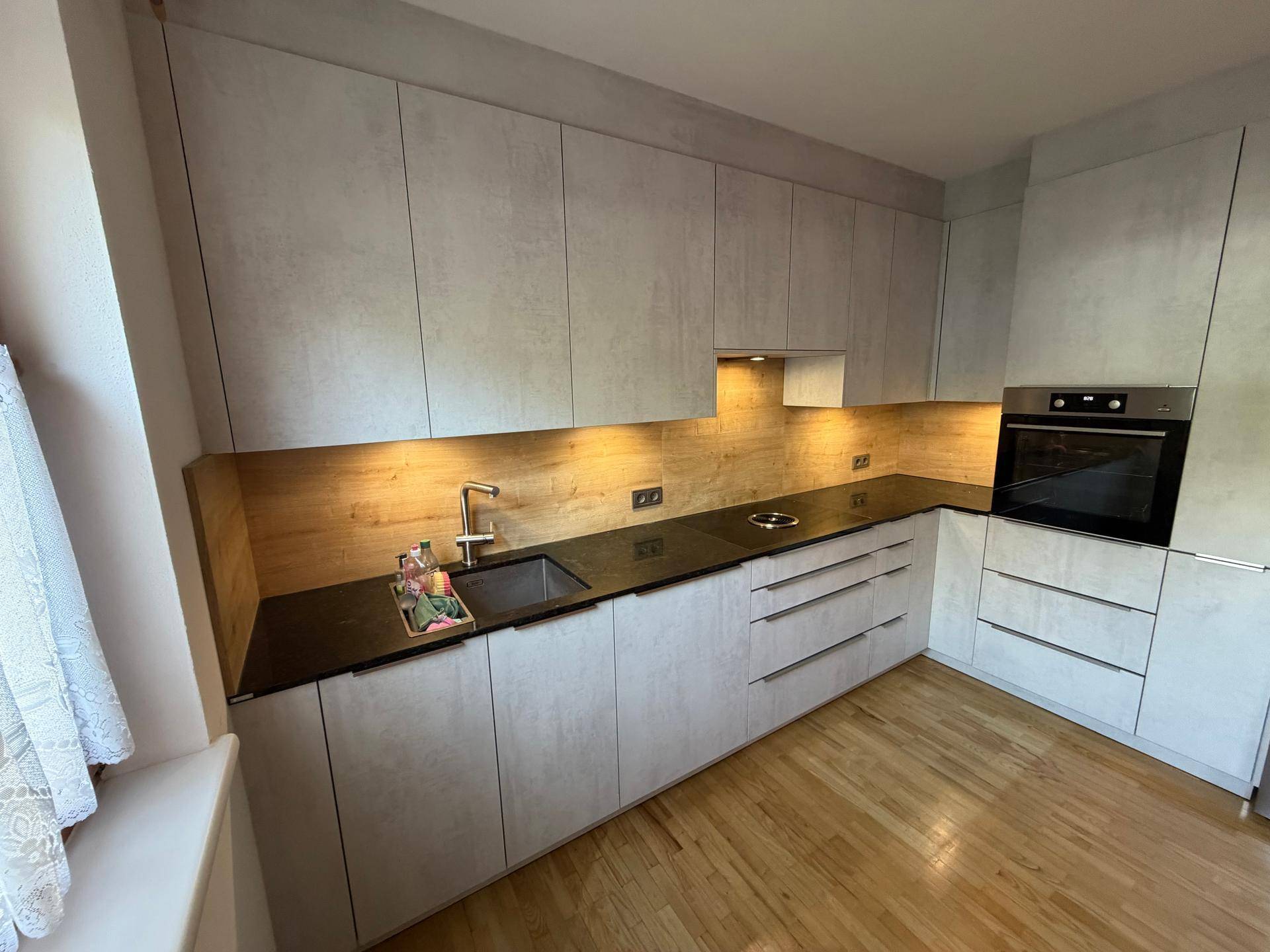 Moderne Einbauküche mit hellgrauen Fronten, dunkler Arbeitsplatte und integriertem Backofen.