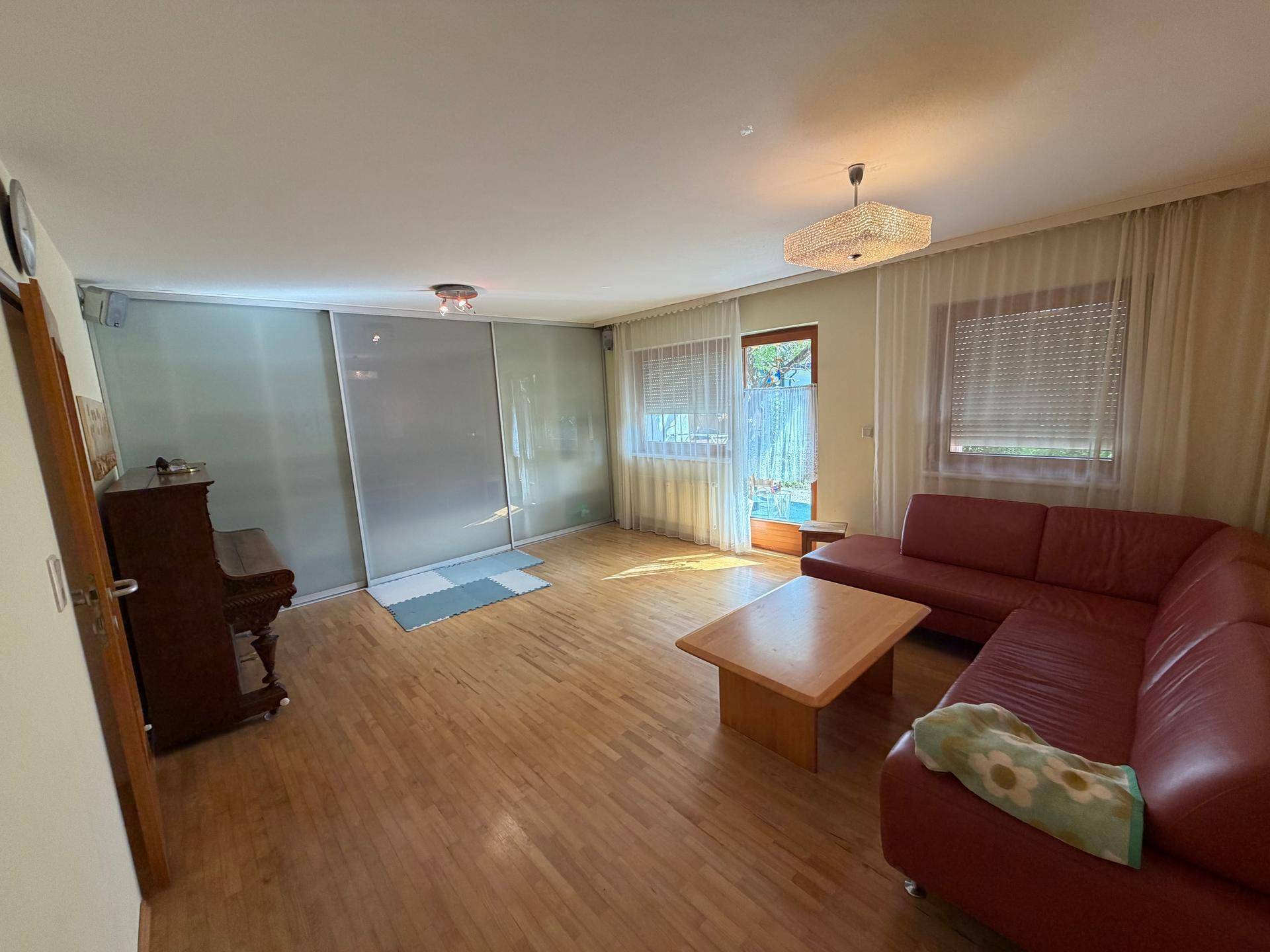 Gemütliches Wohnzimmer mit rotem Sofa, Holzboden und Zugang zur Terrasse oder zum Garten.